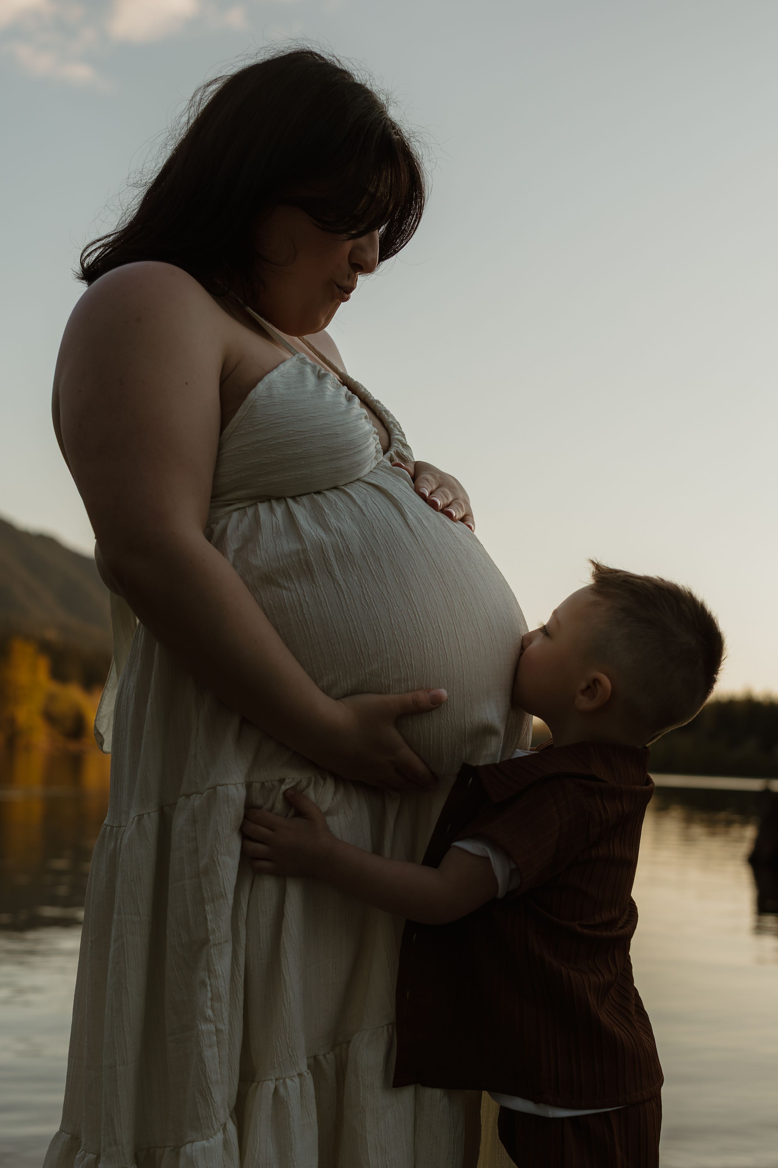 Silhouettes of a parent and child share an emotional embrace against a sunset sky over water.