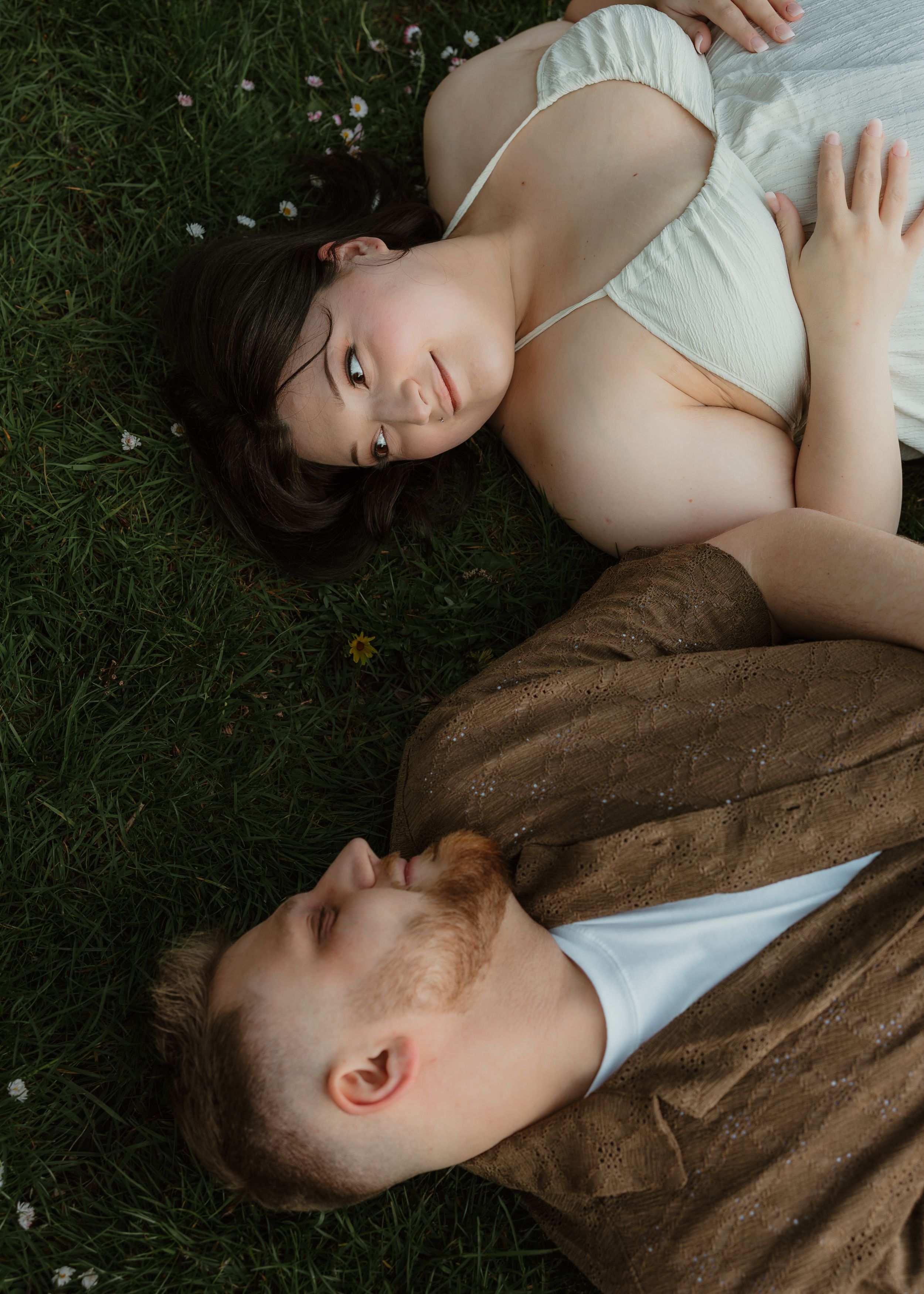 Couple lying on grass sharing intimate moments during a photo shoot.