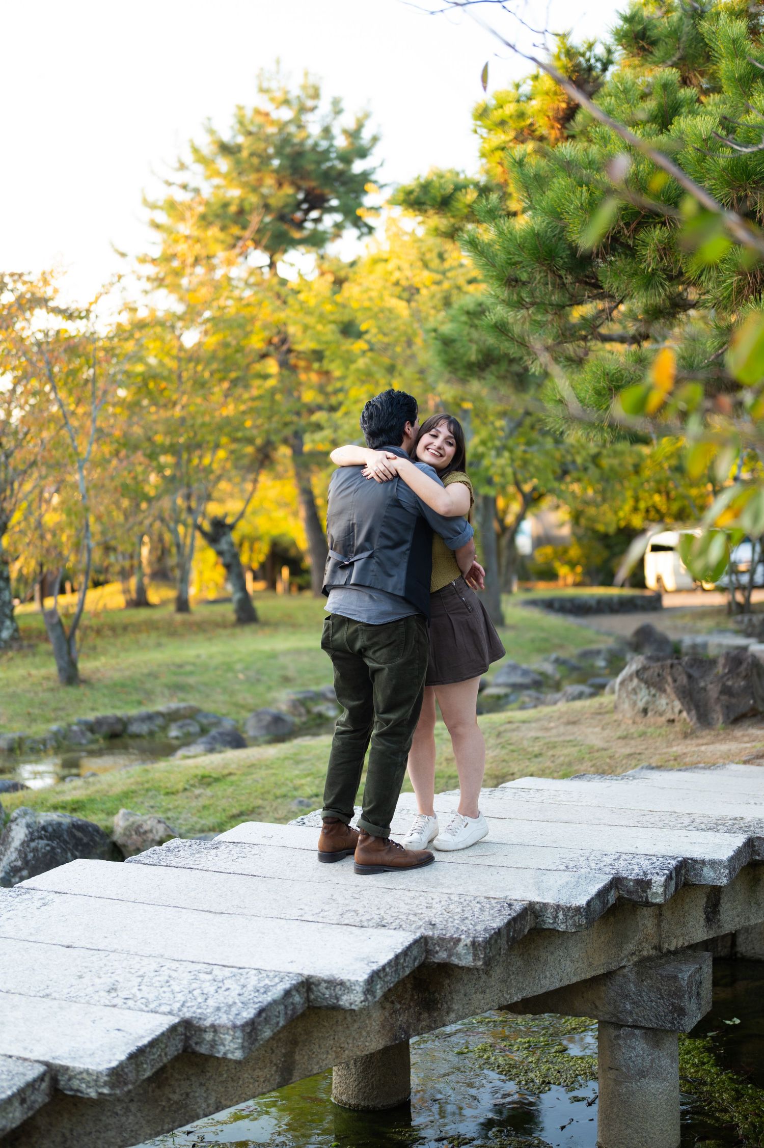 Newly engaged couple hugging joyfully on stone bridge in colorful autumn park.