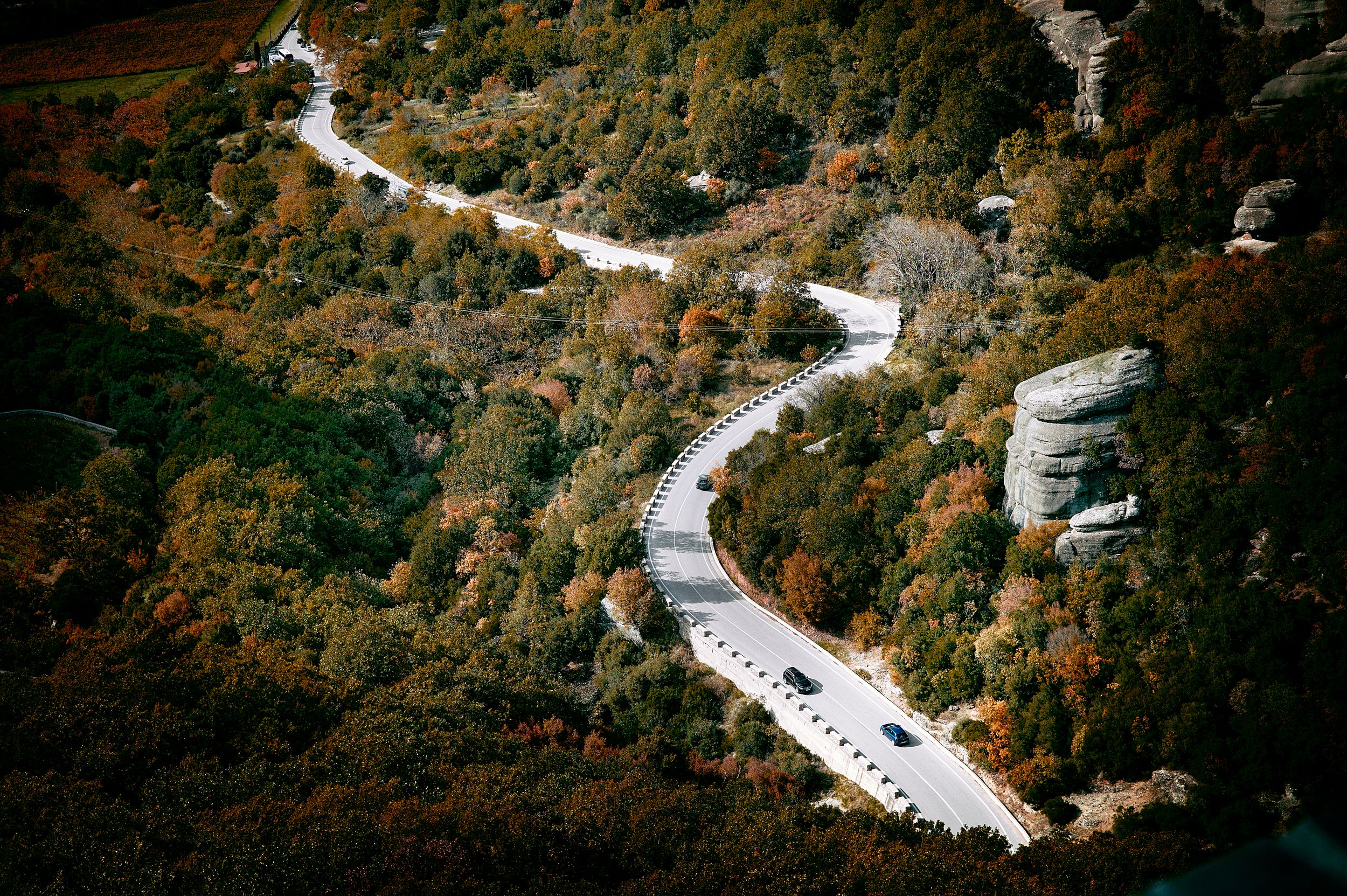 Aerial view of a winding mountain road through dense forest during autumn season.