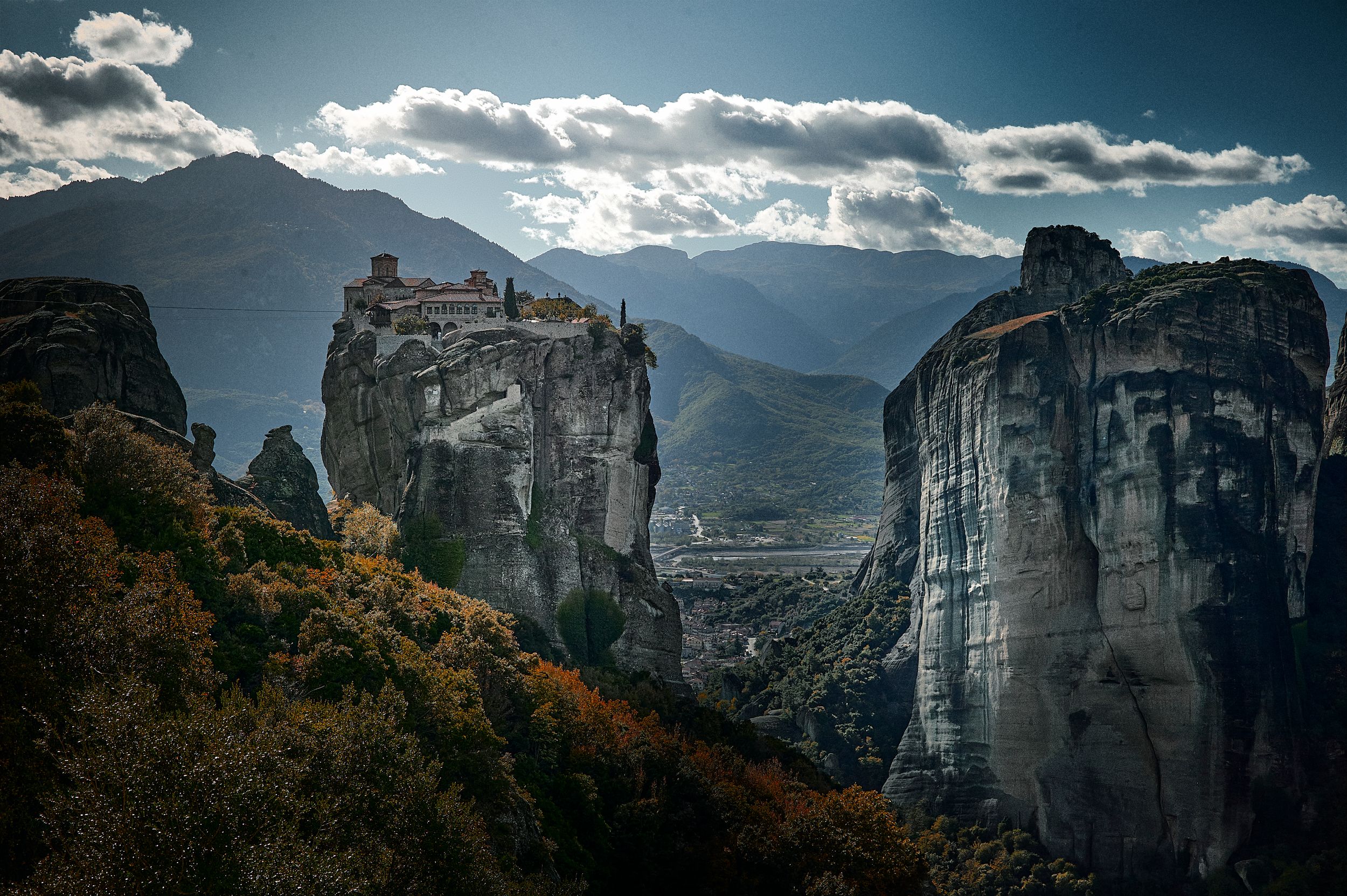 Dramatic panoramic view of Meteora monasteries perched atop towering rock formations in Greece at sunset.