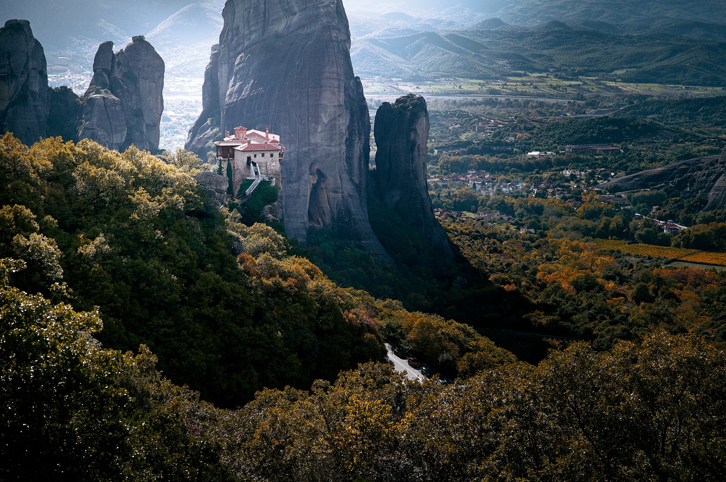 Dramatic aerial view of Meteora monasteries perched atop towering rock formations in Greece during golden sunset.