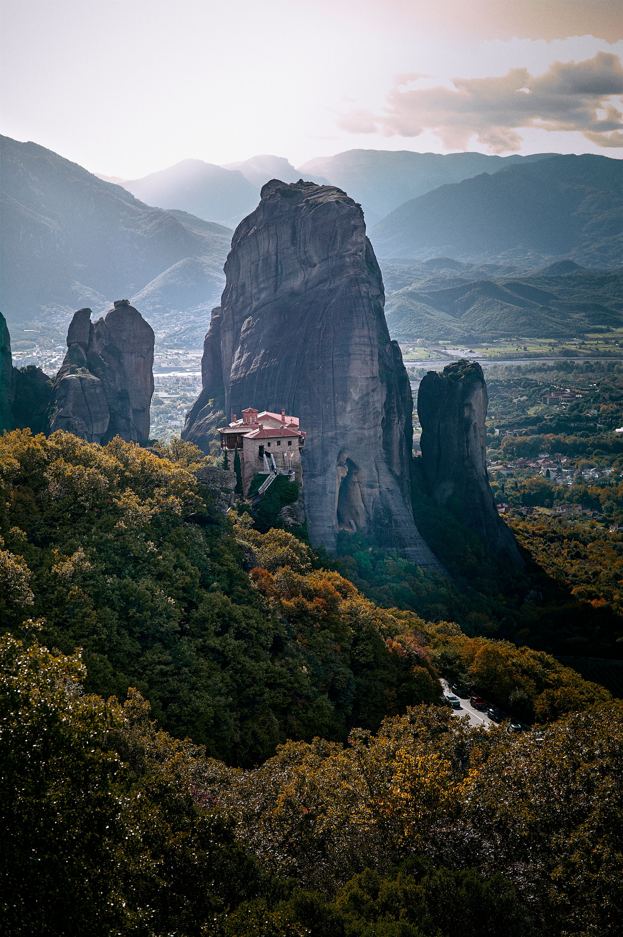 Dramatic view of Meteora's towering sandstone cliffs with monasteries perched on top during golden hour in Greece.