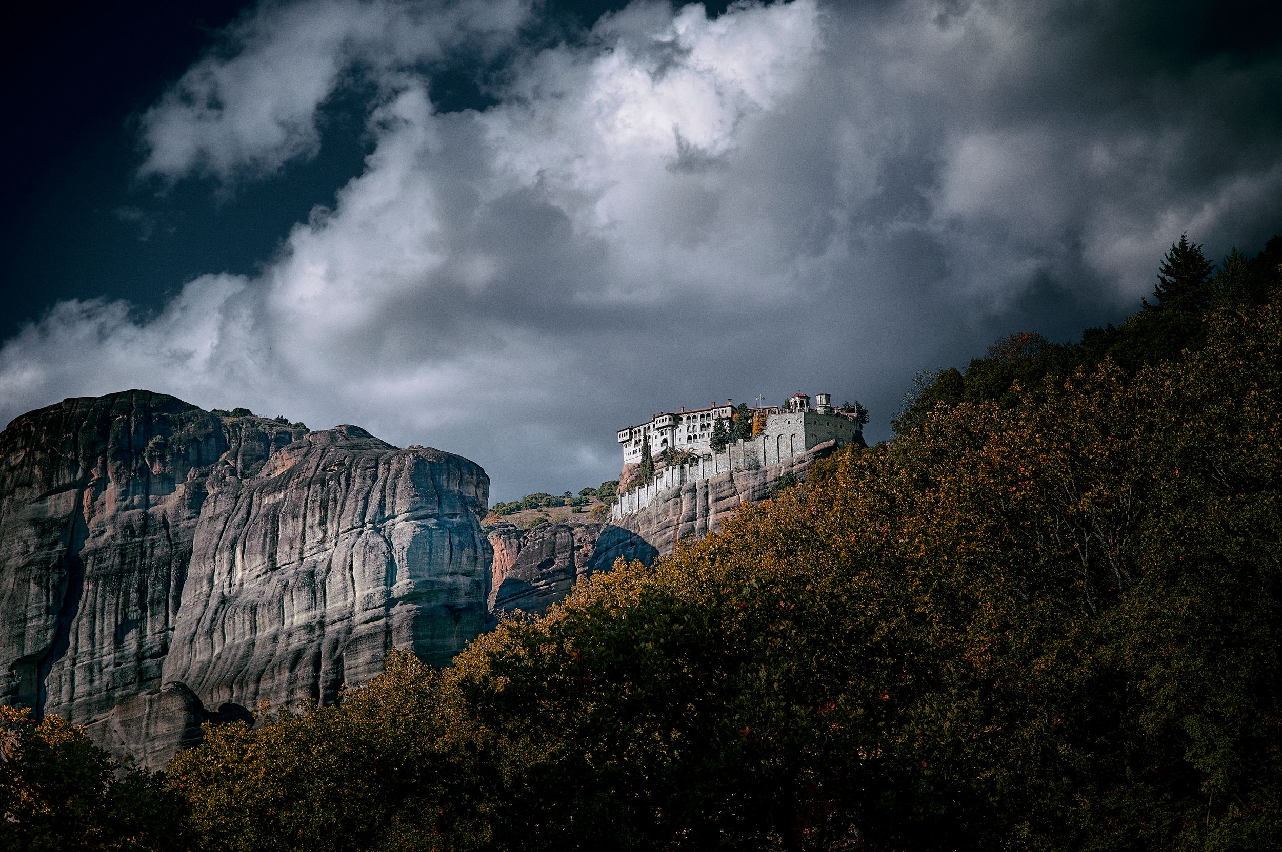A dramatic view of Meteora monasteries perched atop steep cliffs in Greece under moody storm clouds.