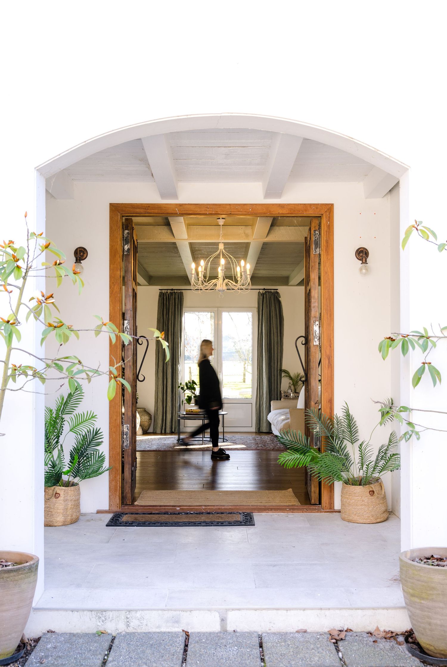 Modern home entrance with white columns, glass doors, and potted plants creates an elegant covered patio walkway.
