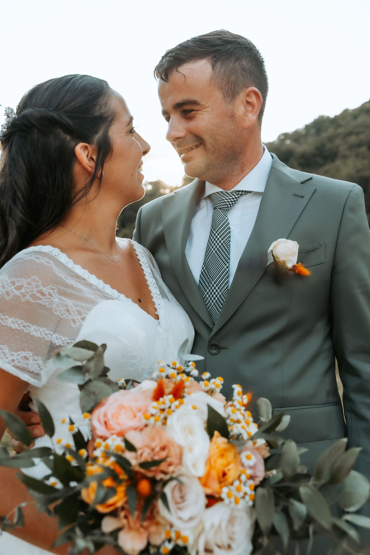 Newlyweds with vibrant orange and peach floral bouquet in an outdoor setting.