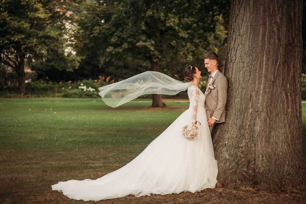 Bride's flowing white wedding dress veil catches the wind gracefully in an outdoor garden setting.