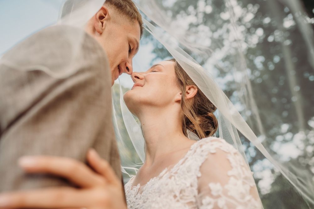 A romantic couple shares a tender kiss in a dreamy outdoor setting with blossoming trees in the background.