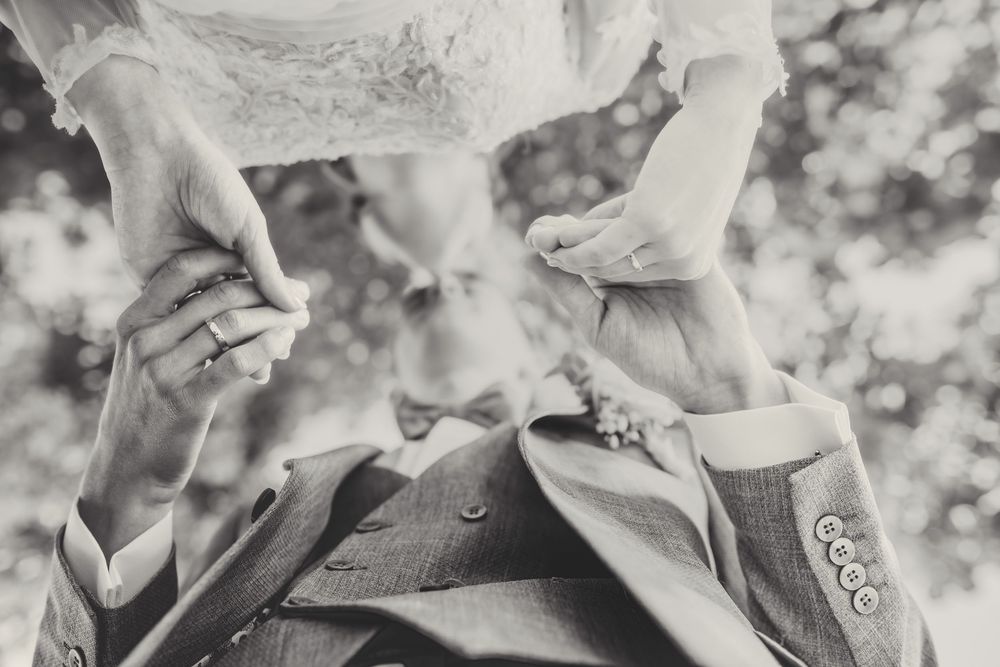 A close-up black and white photograph shows hands carefully folding origami paper into intricate shapes.