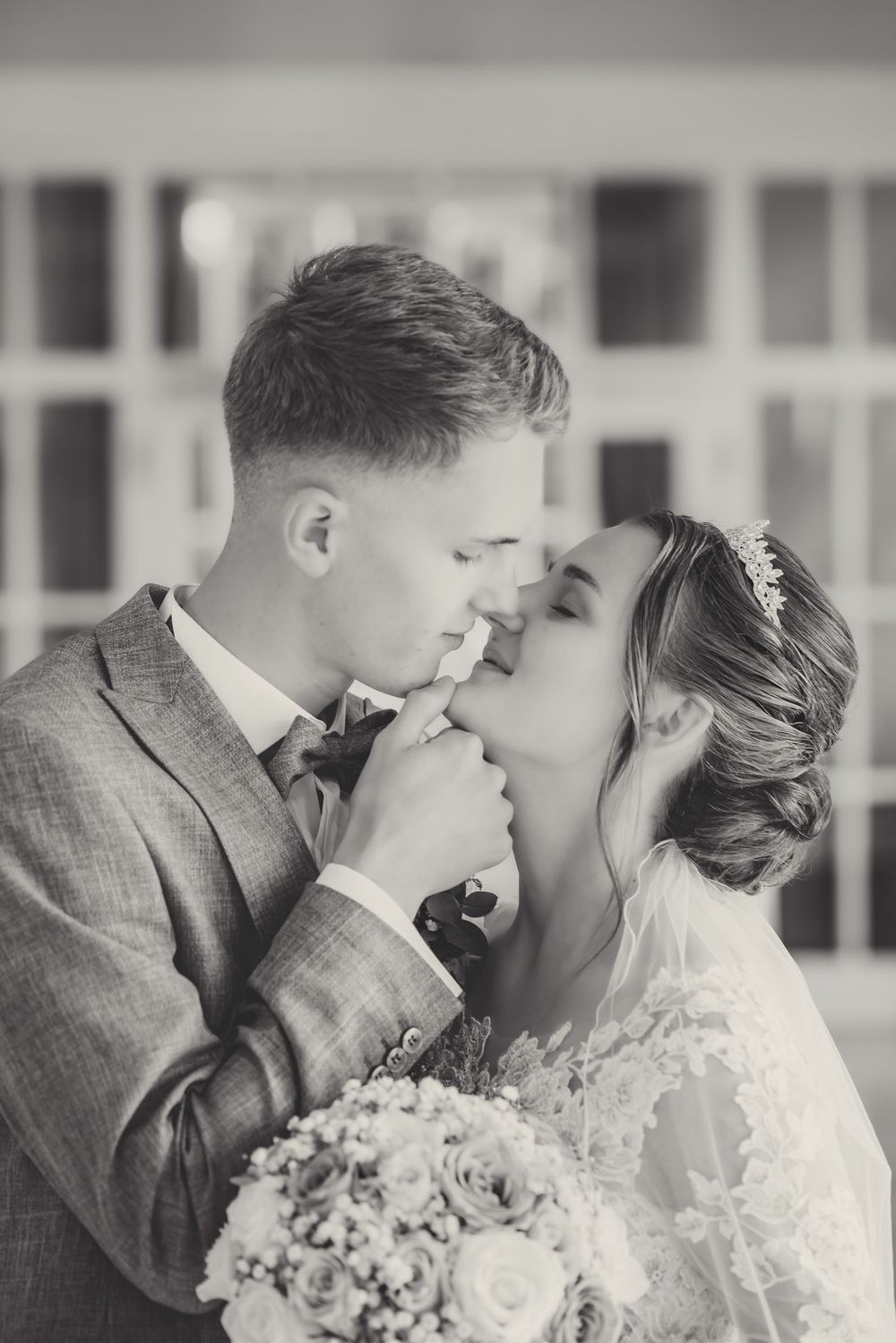 A romantic black and white wedding photo series showing tender kisses between a couple in formal attire with flowers.