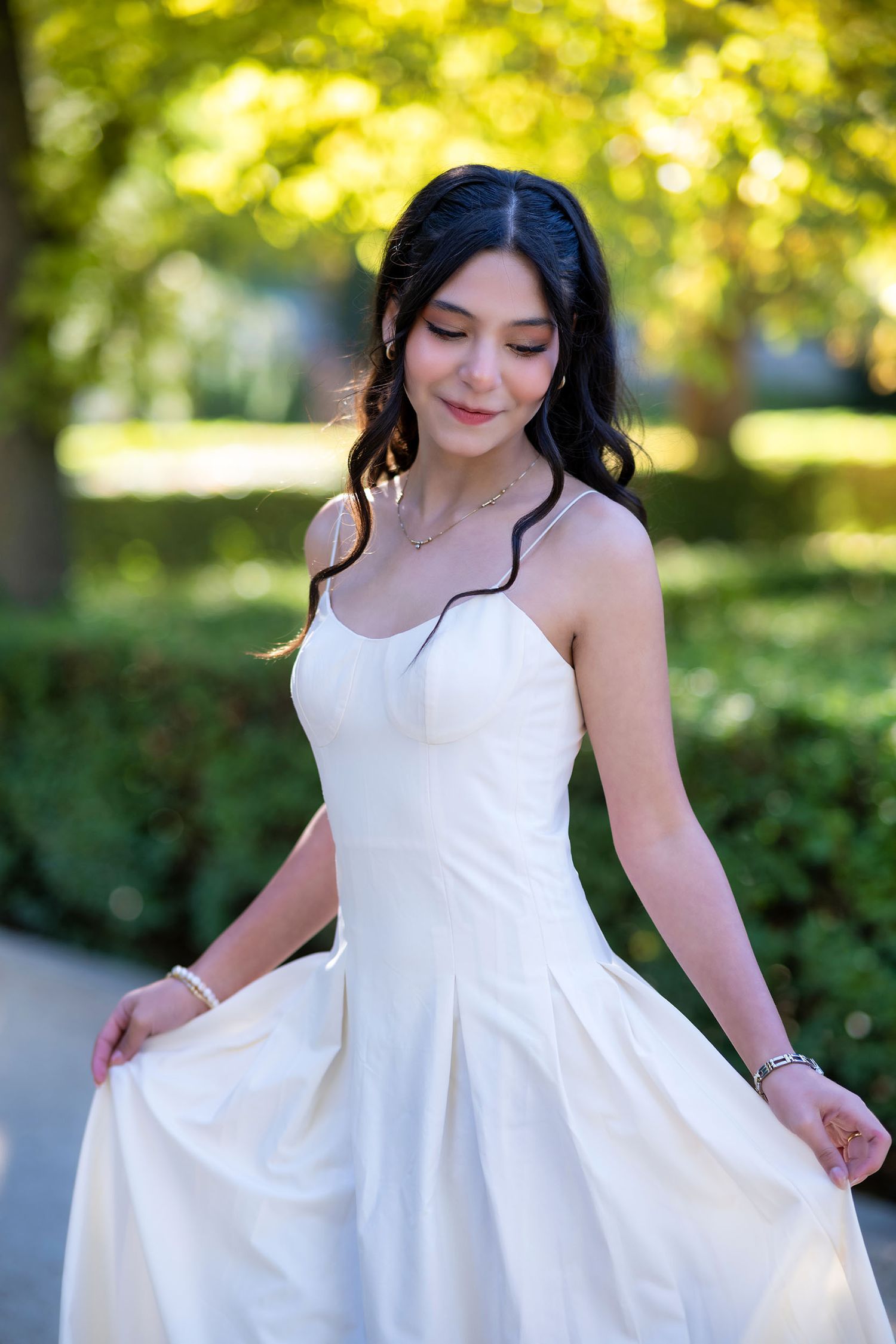 A woman in a flowing white dress twirls gracefully in a sun-dappled garden setting.