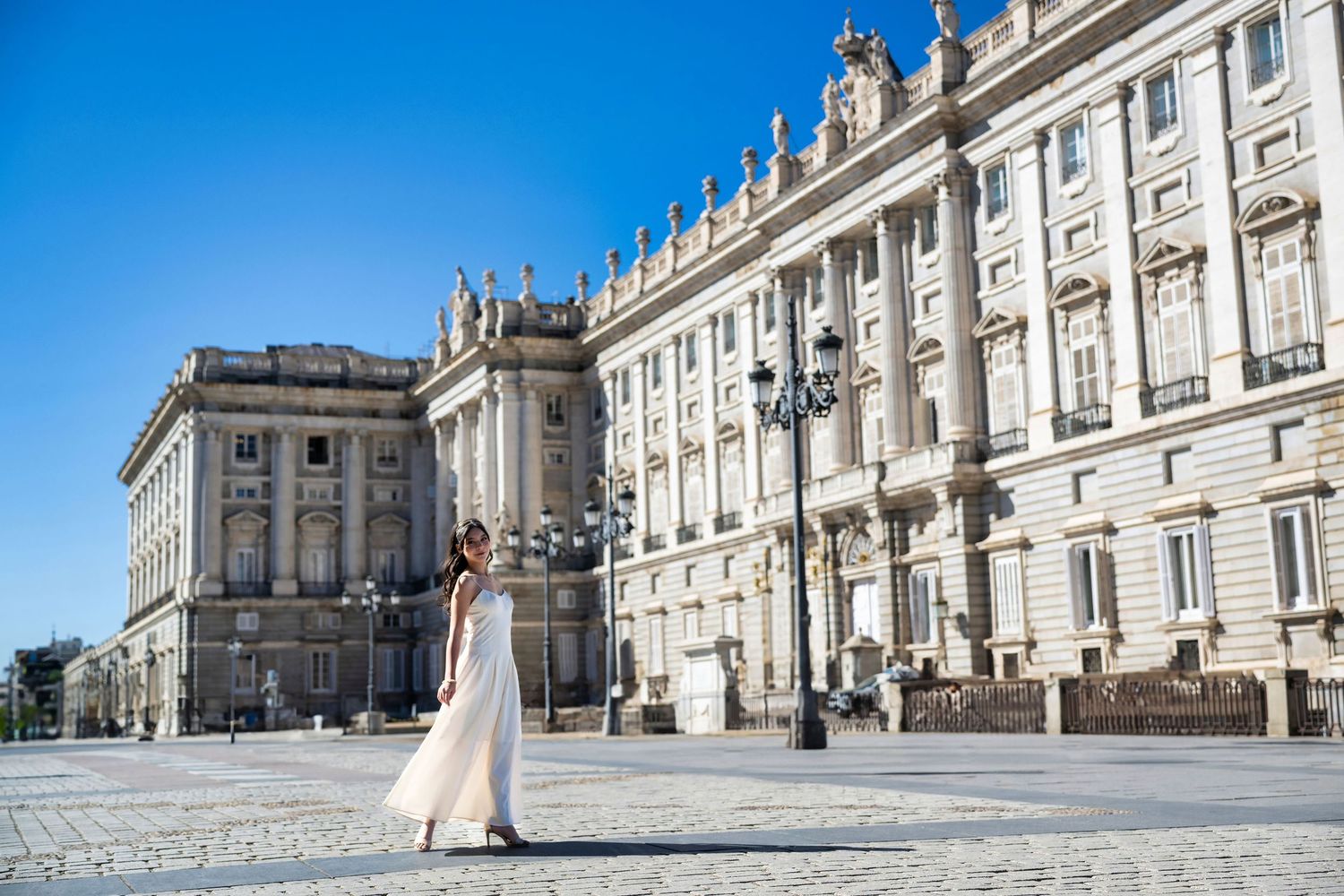Elegant wedding couple poses at the Royal Palace of Madrid with its grand Baroque architecture in the background.