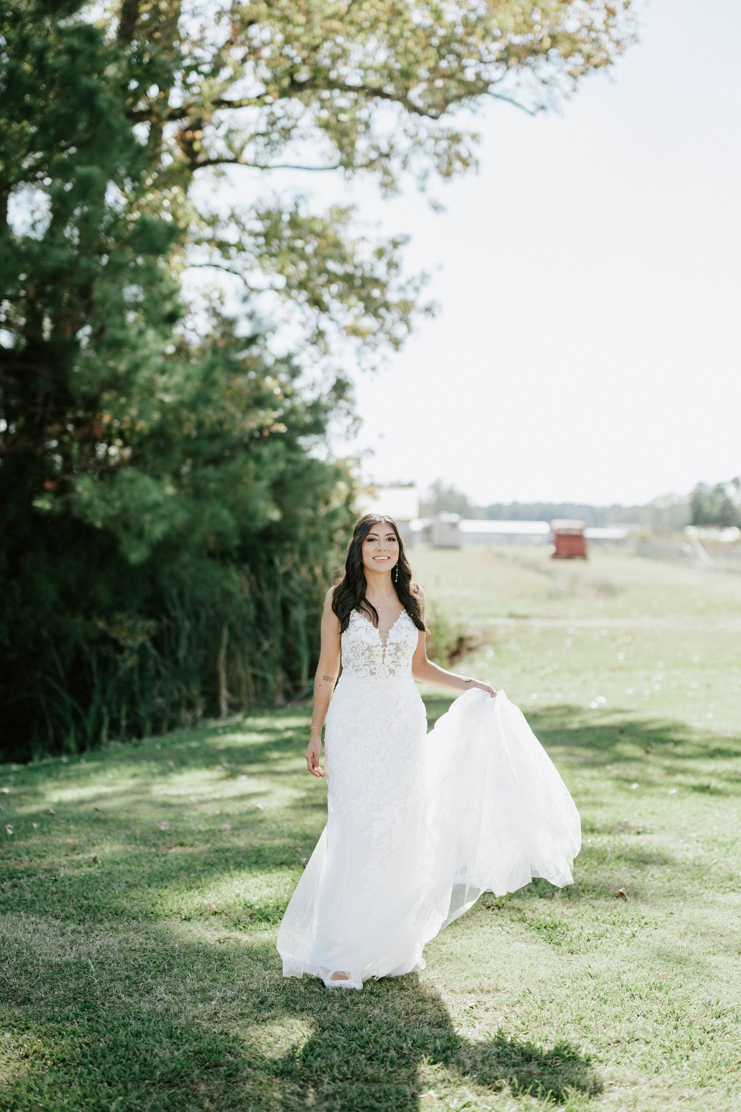 A flowing white wedding dress twirls gracefully in a sunny meadow with trees in the background.