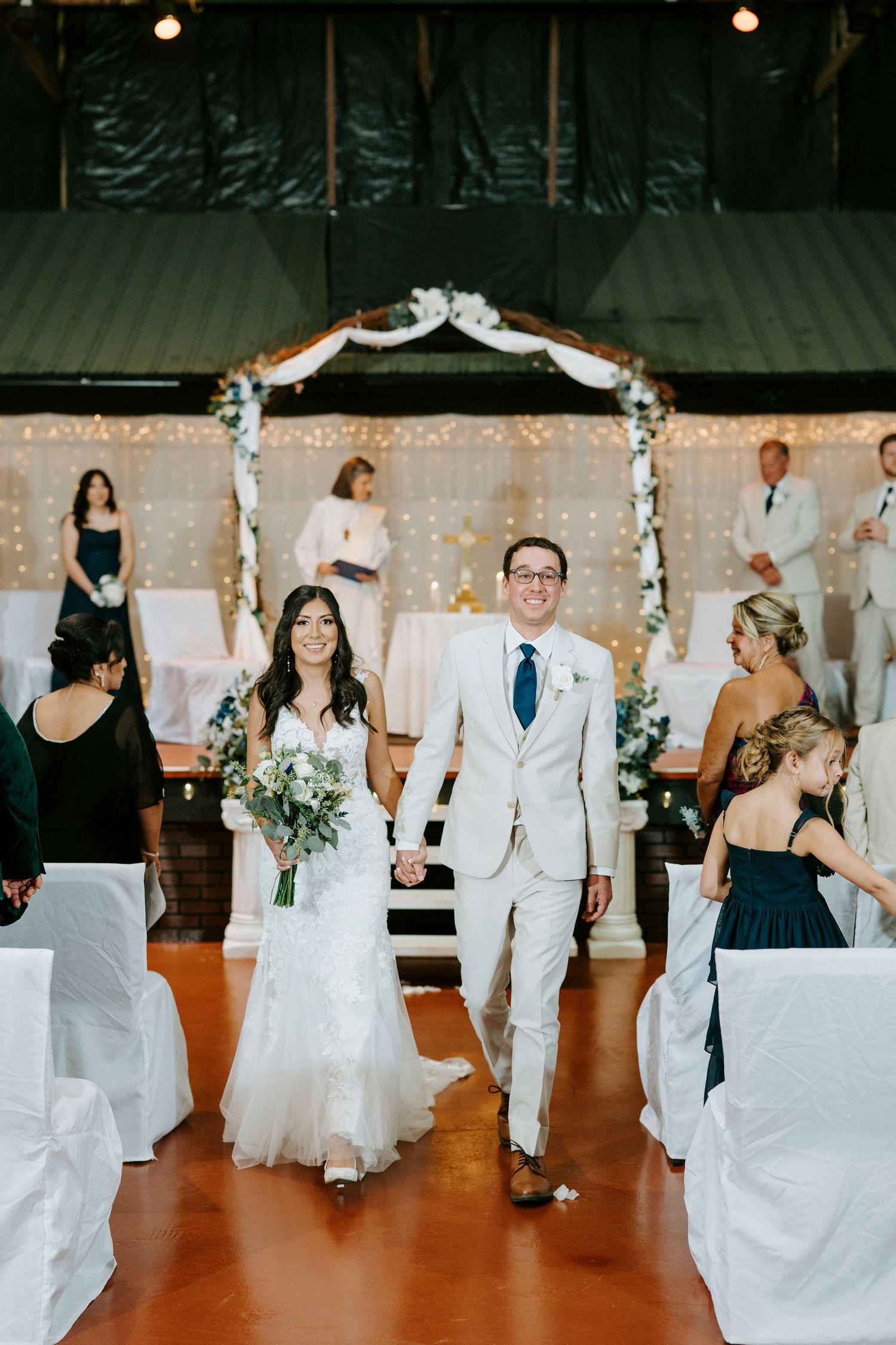 Wedding party members dance in a line on a wooden floor at reception while wearing white and black formal attire.