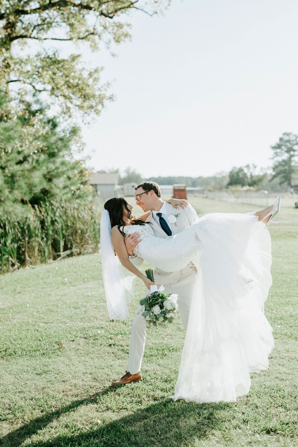 A romantic wedding couple dances and twirls together on a sunlit grassy hillside with flowing white dress and suit.