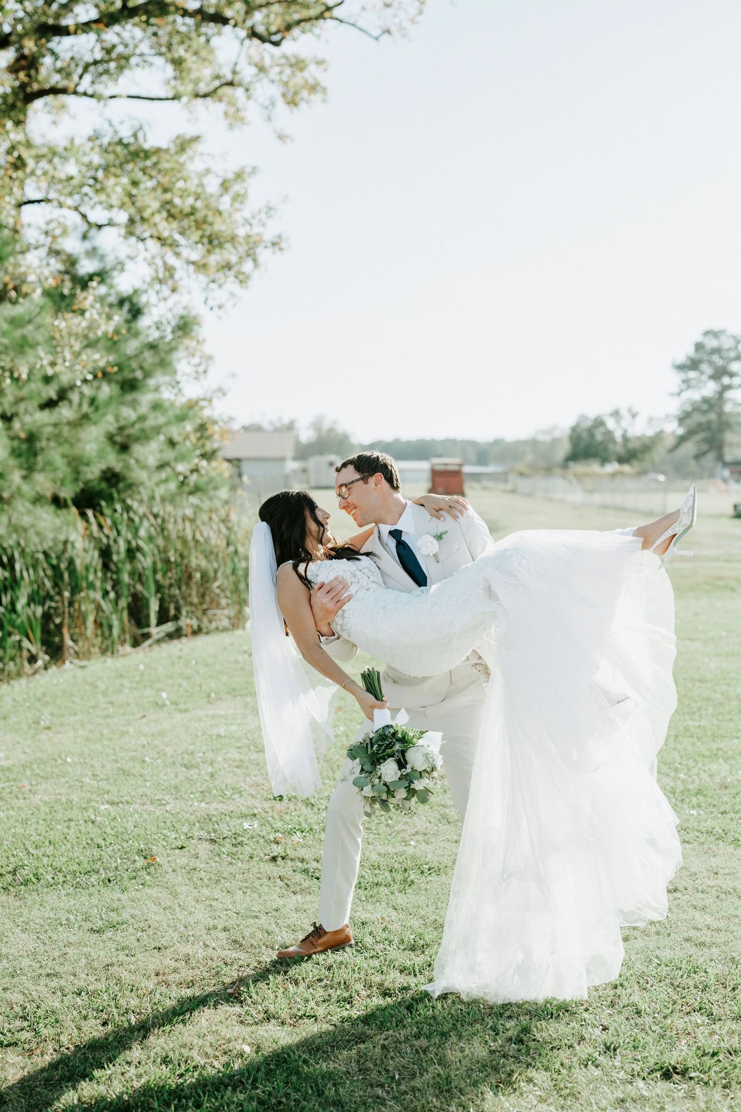 A romantic wedding couple dances and twirls together on a sunlit grassy hillside with flowing white dress and suit.