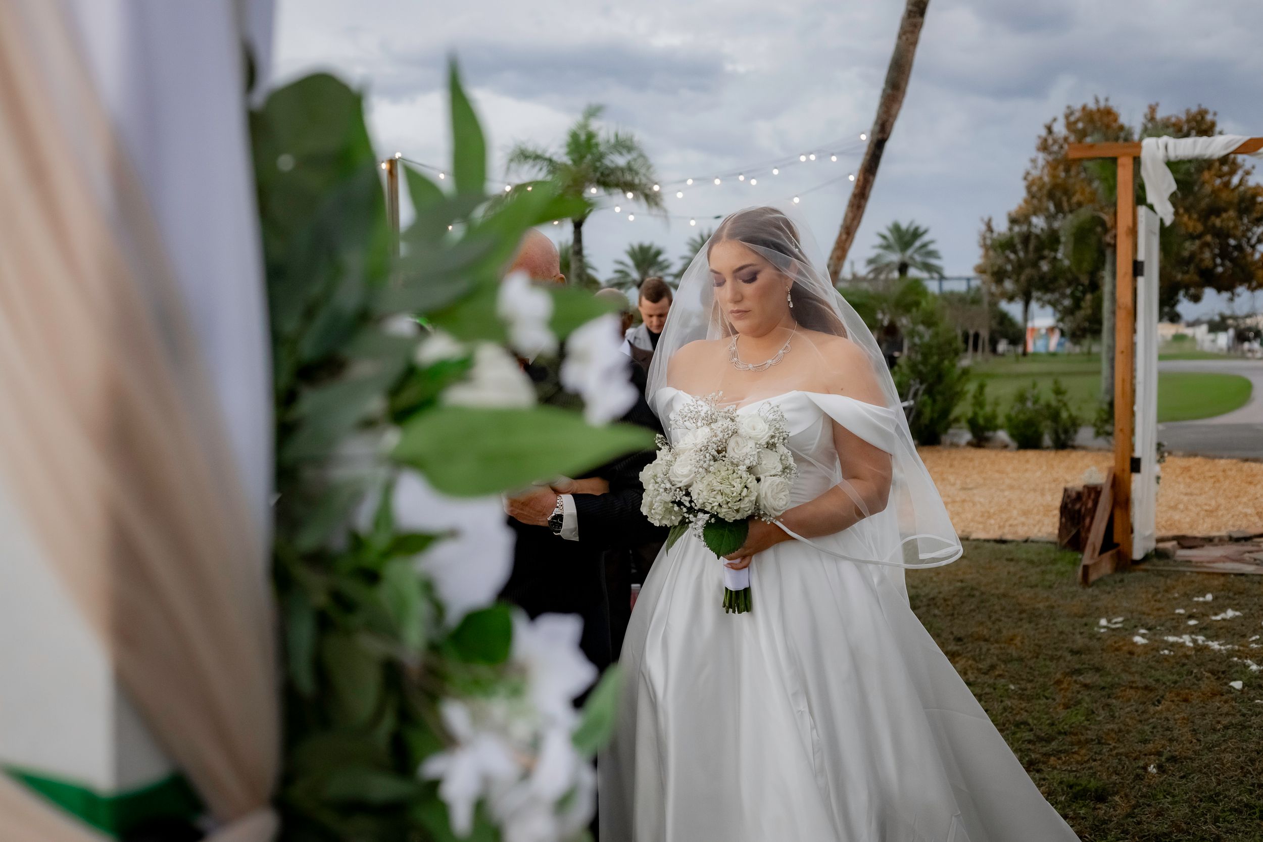 Elegant outdoor wedding ceremony setup with white draping and palm trees in a tropical setting.