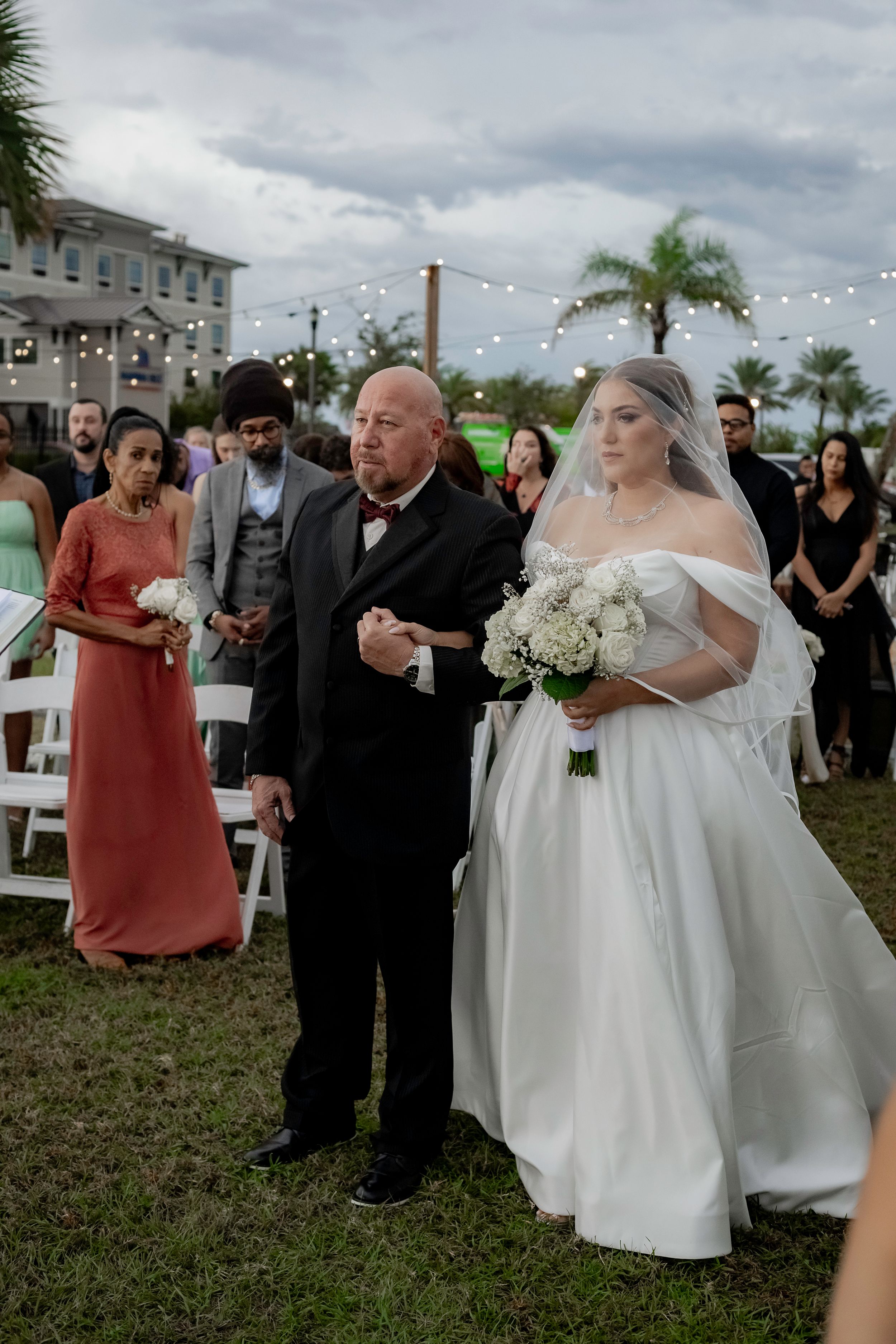 Outdoor wedding ceremony with guests gathered on grass under cloudy sky.