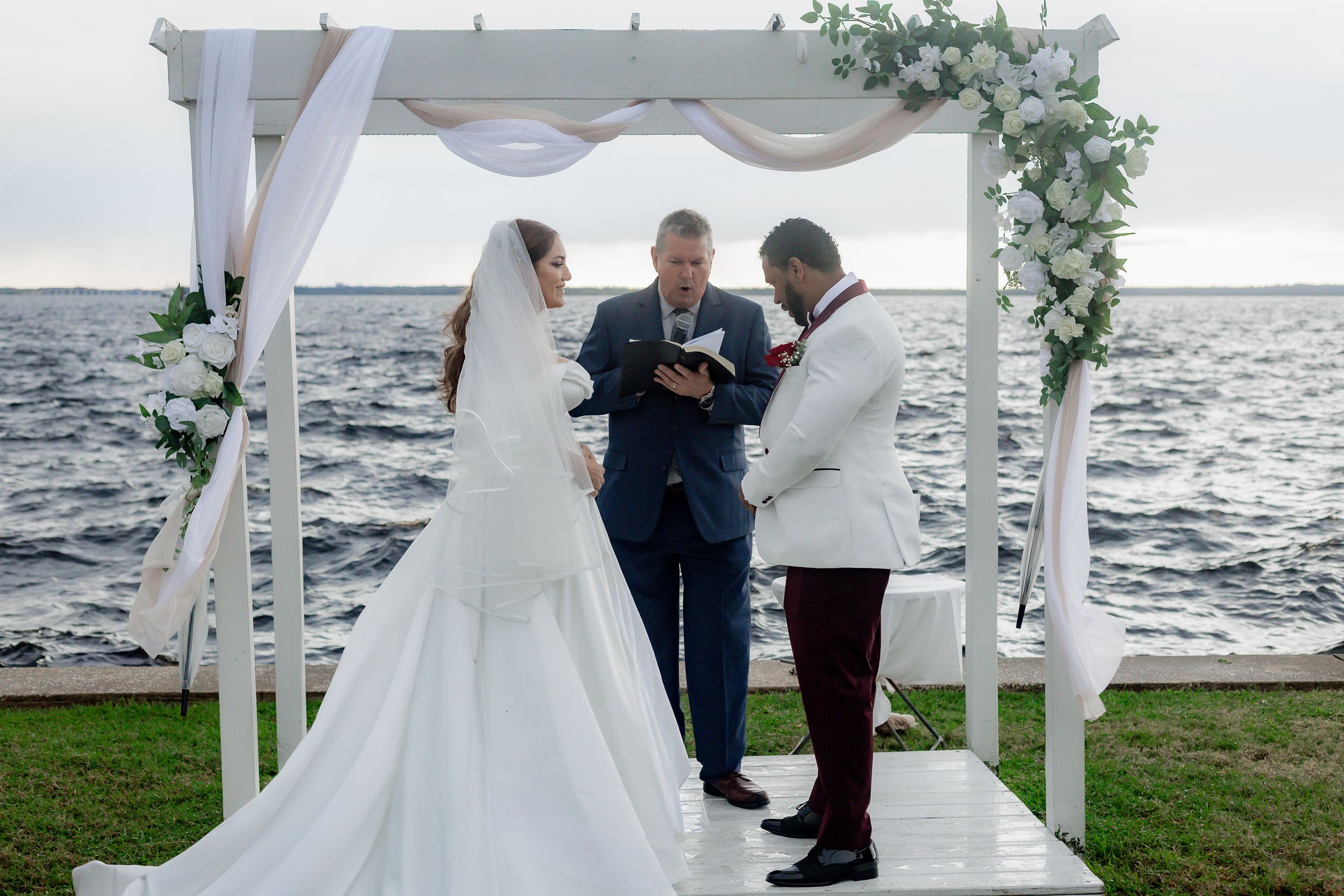 A romantic waterfront wedding ceremony setup with white chairs and floral arch overlooking the ocean.