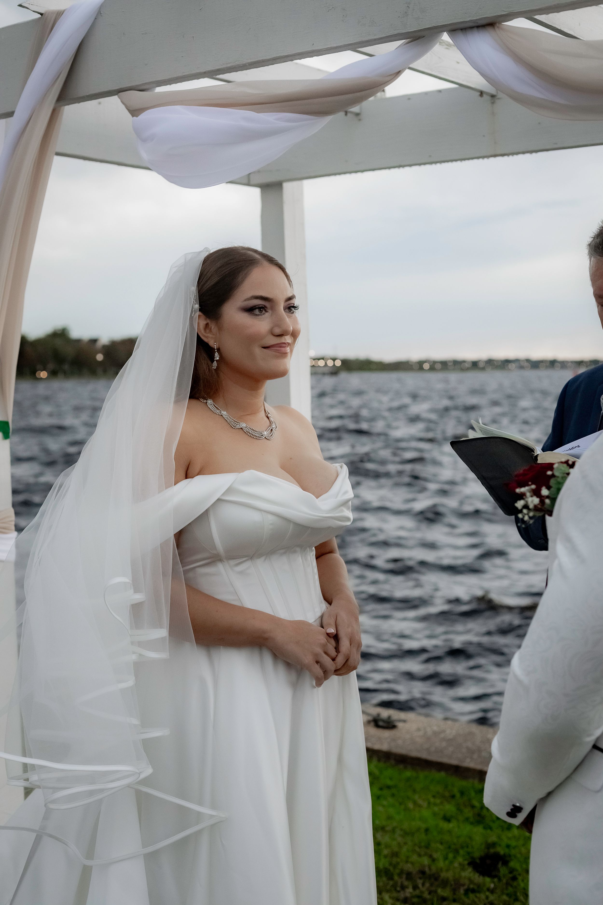 An elegant waterfront wedding ceremony with white decor and flowing fabric against a scenic lake backdrop.