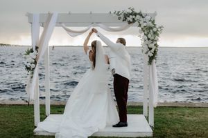 Beachside wedding ceremony under a white draped arch with ocean views.