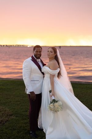 Elegant beachside wedding ceremony at sunset with white dress and burgundy accents.