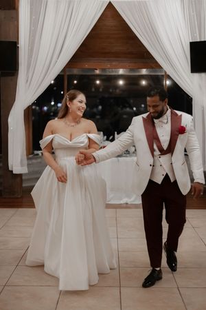 Wedding couple dancing together on white tiled floor under draped fabric ceiling.
