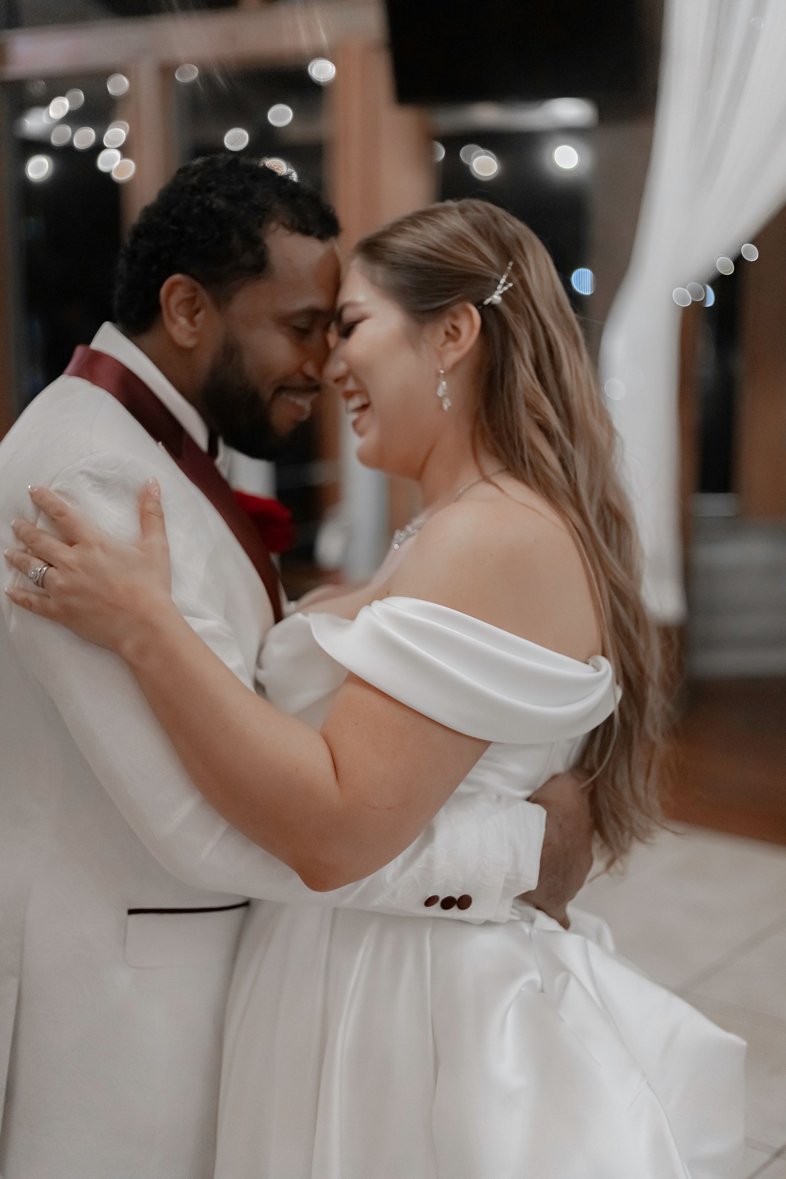 A romantic wedding couple shares an intimate dance moment under twinkling lights at their reception.