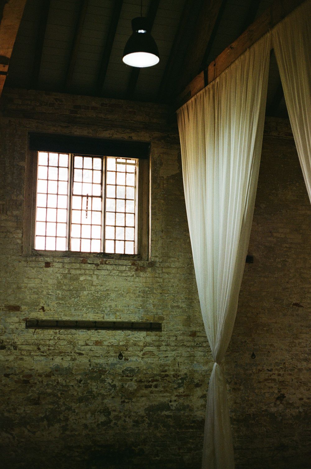 moody film wedding detail Interior of rustic brick warehouse with white flowing curtains and industrial windows creating moody ambiance.