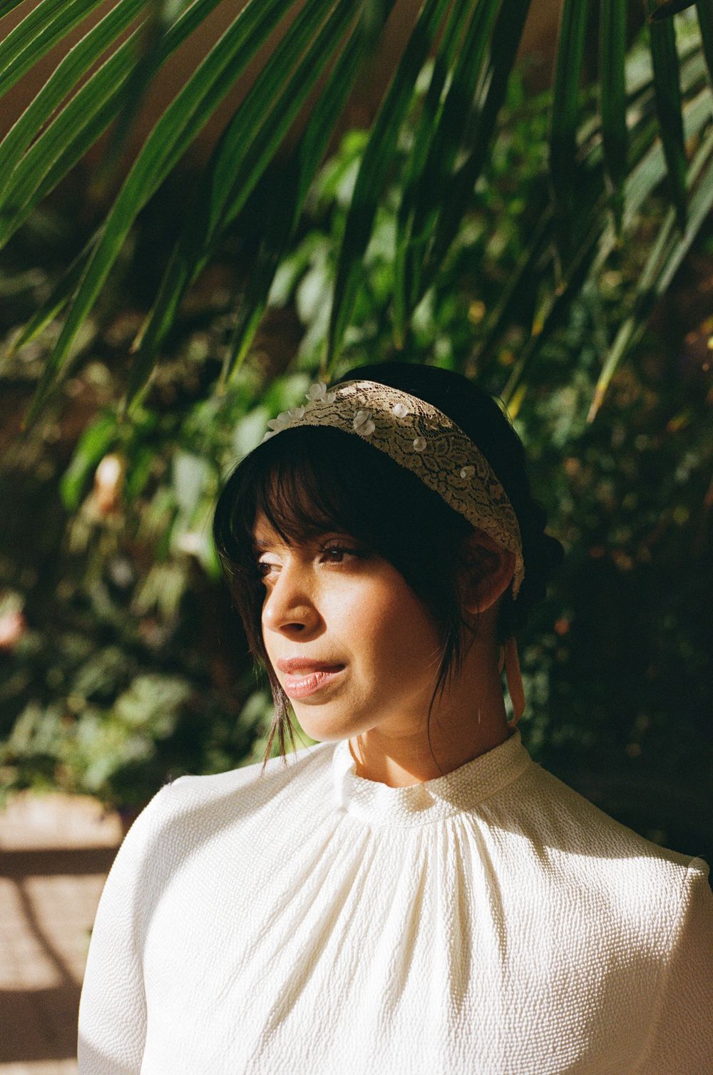 A dreamy portrait in a conservatory with palm fronds and natural light creating soft shadows and highlights.