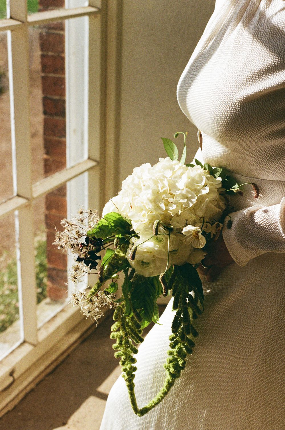 nostalgic wedding film moment of hydrangea flowers in a rustic window frame create an elegant vintage vignette against exposed brick wall.