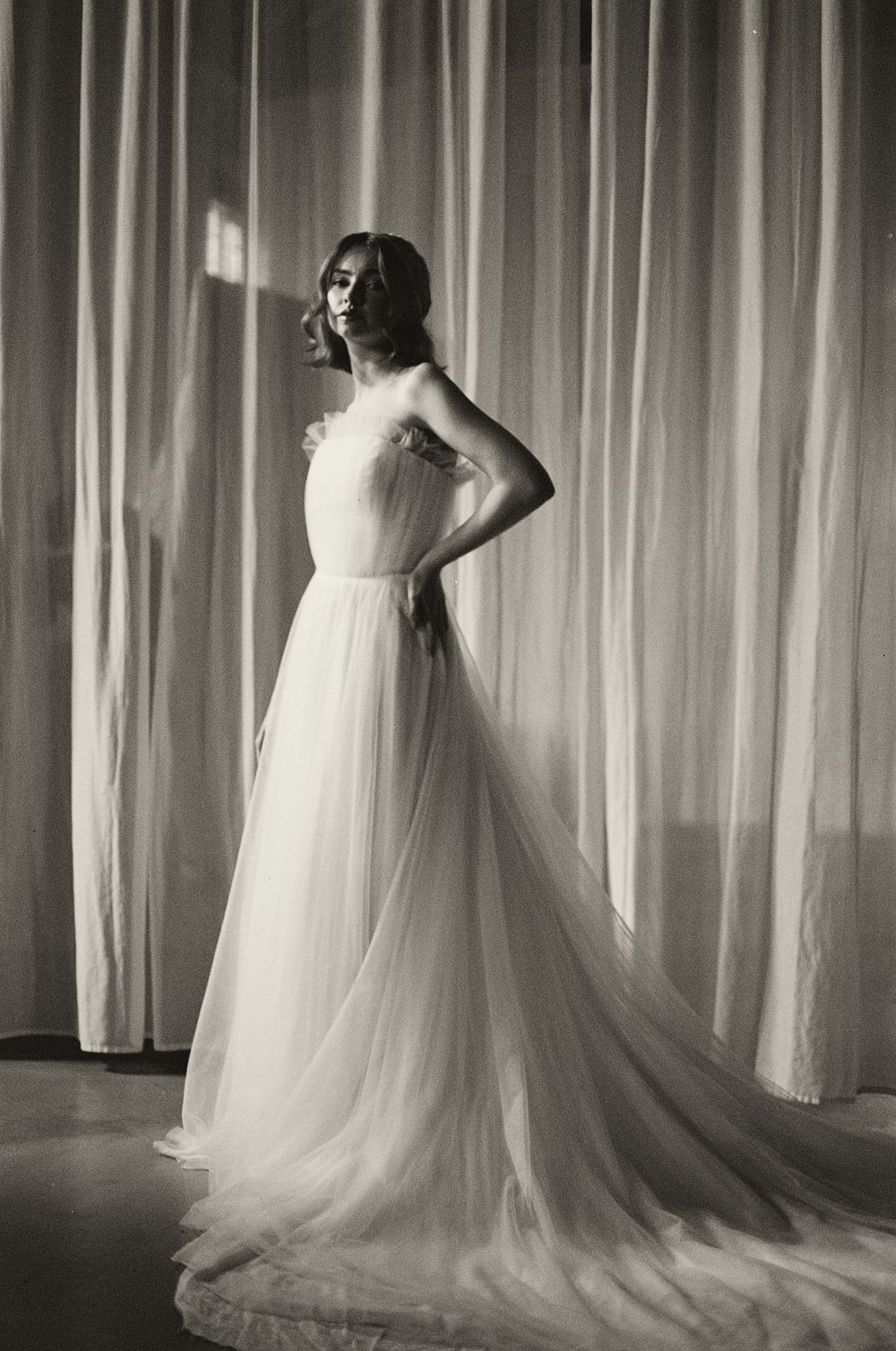35mm film wedding portrait flowing white wedding dress with tulle skirt against a curtained backdrop.