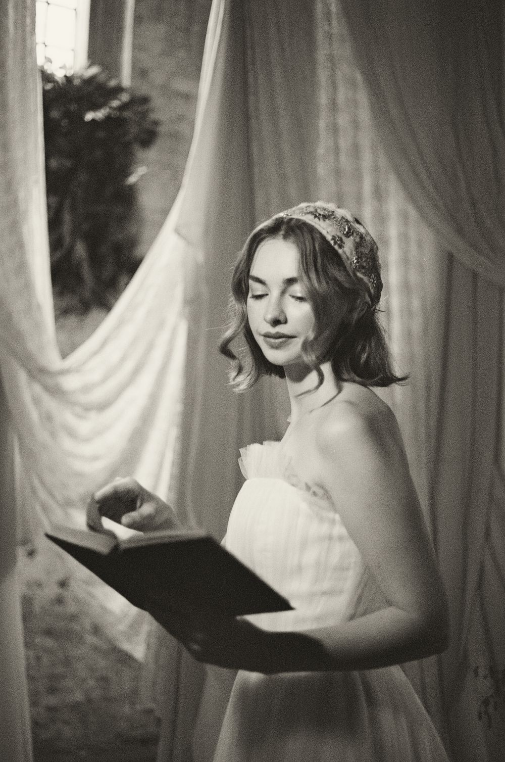 Black and white artistic photo series showing a person in soft lighting reading near flowing white curtains.
