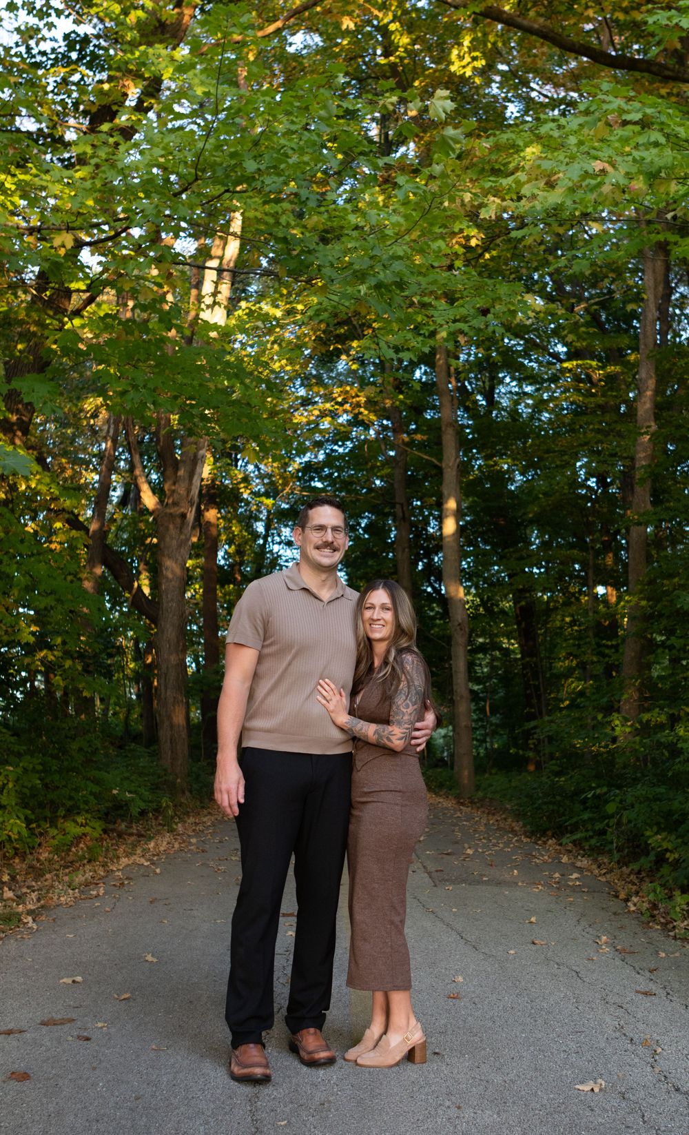 Couple stands together on a tree-lined path during autumn.