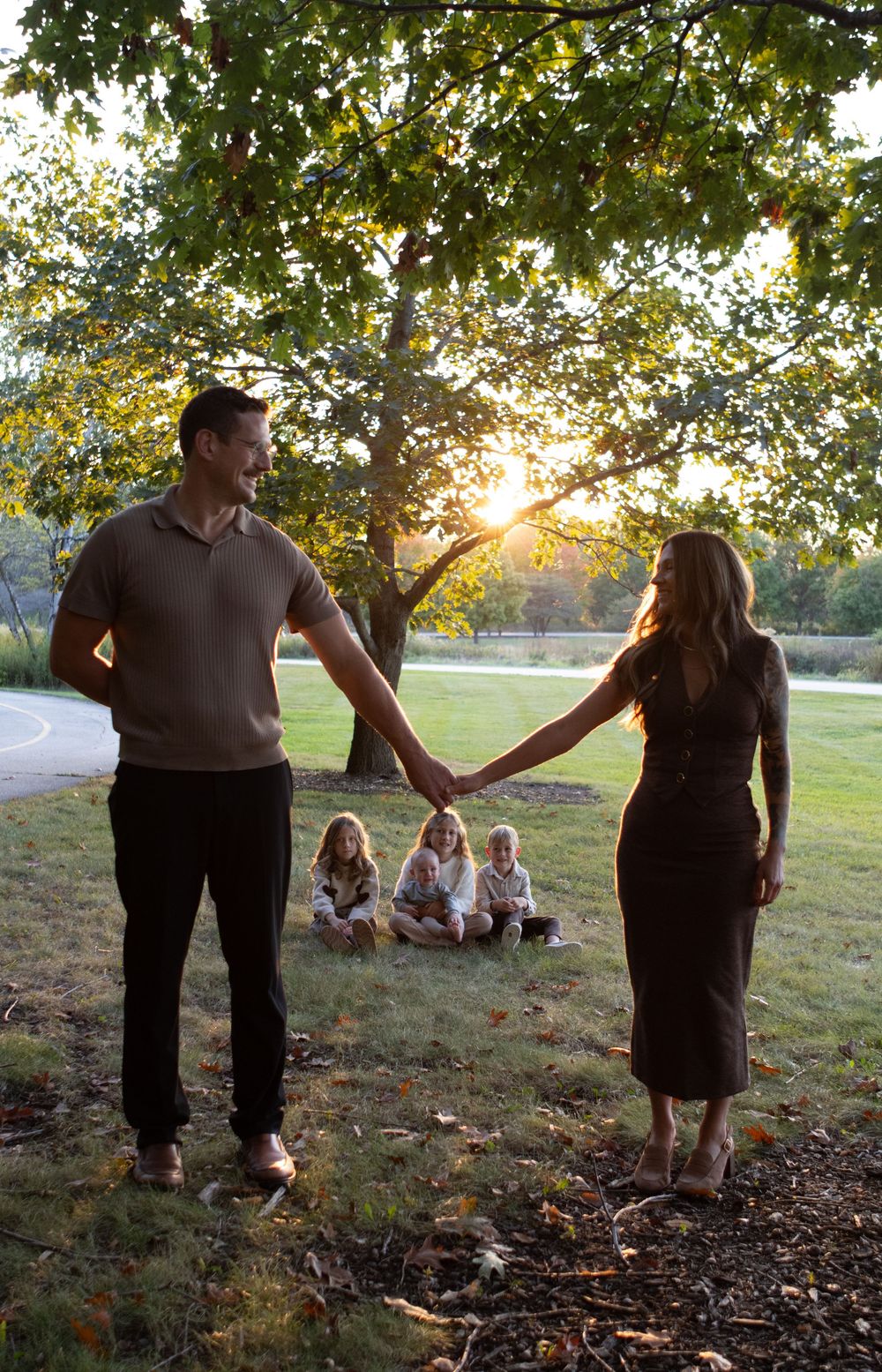 People holding hands while standing on a grassy slope at sunset near a lake.