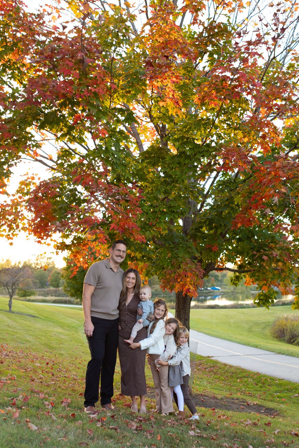 Family portrait session under vibrant autumn trees with golden leaves and a winding path in the background.