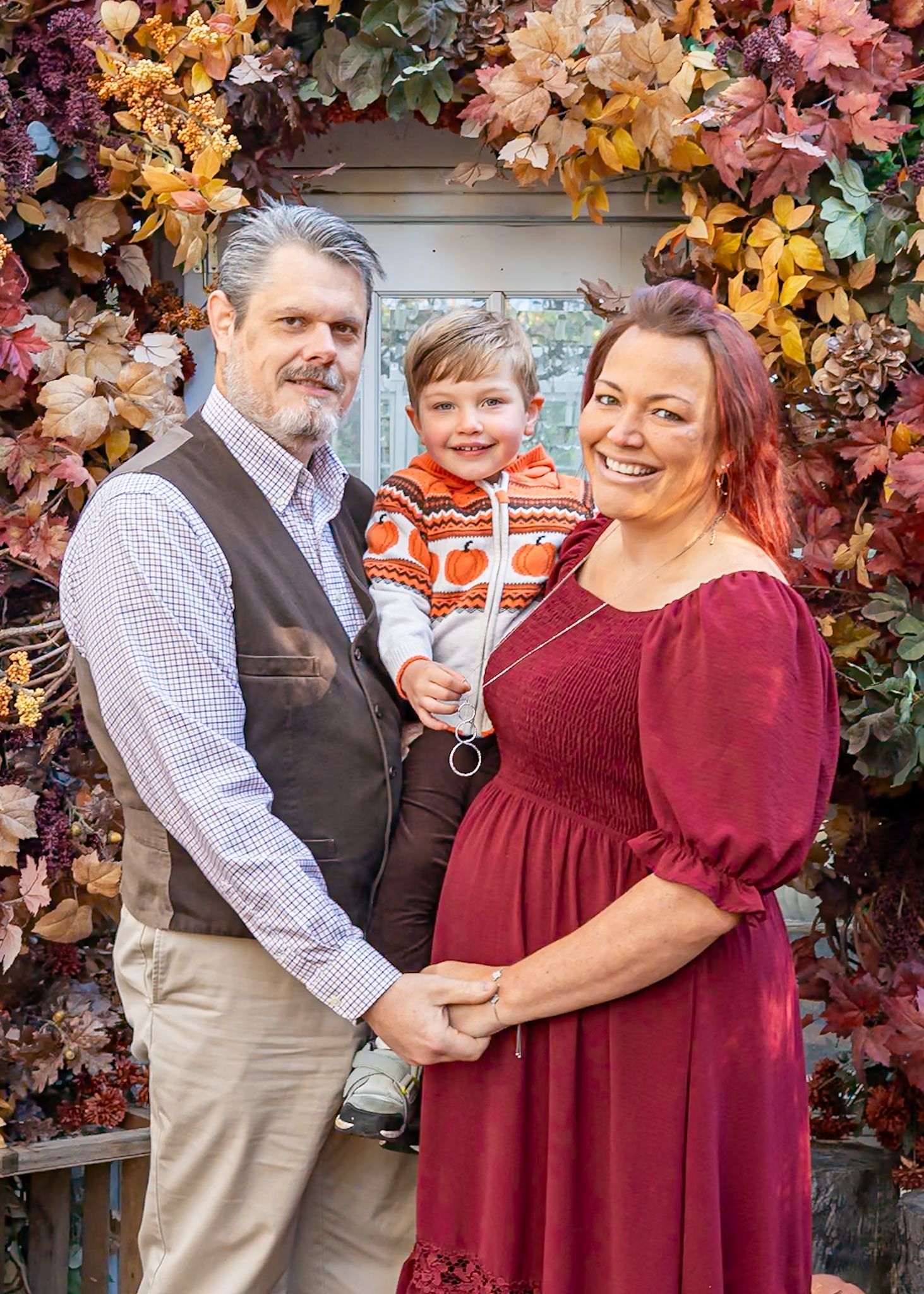 A couple embraces in front of colorful autumn foliage wearing burgundy and plaid.