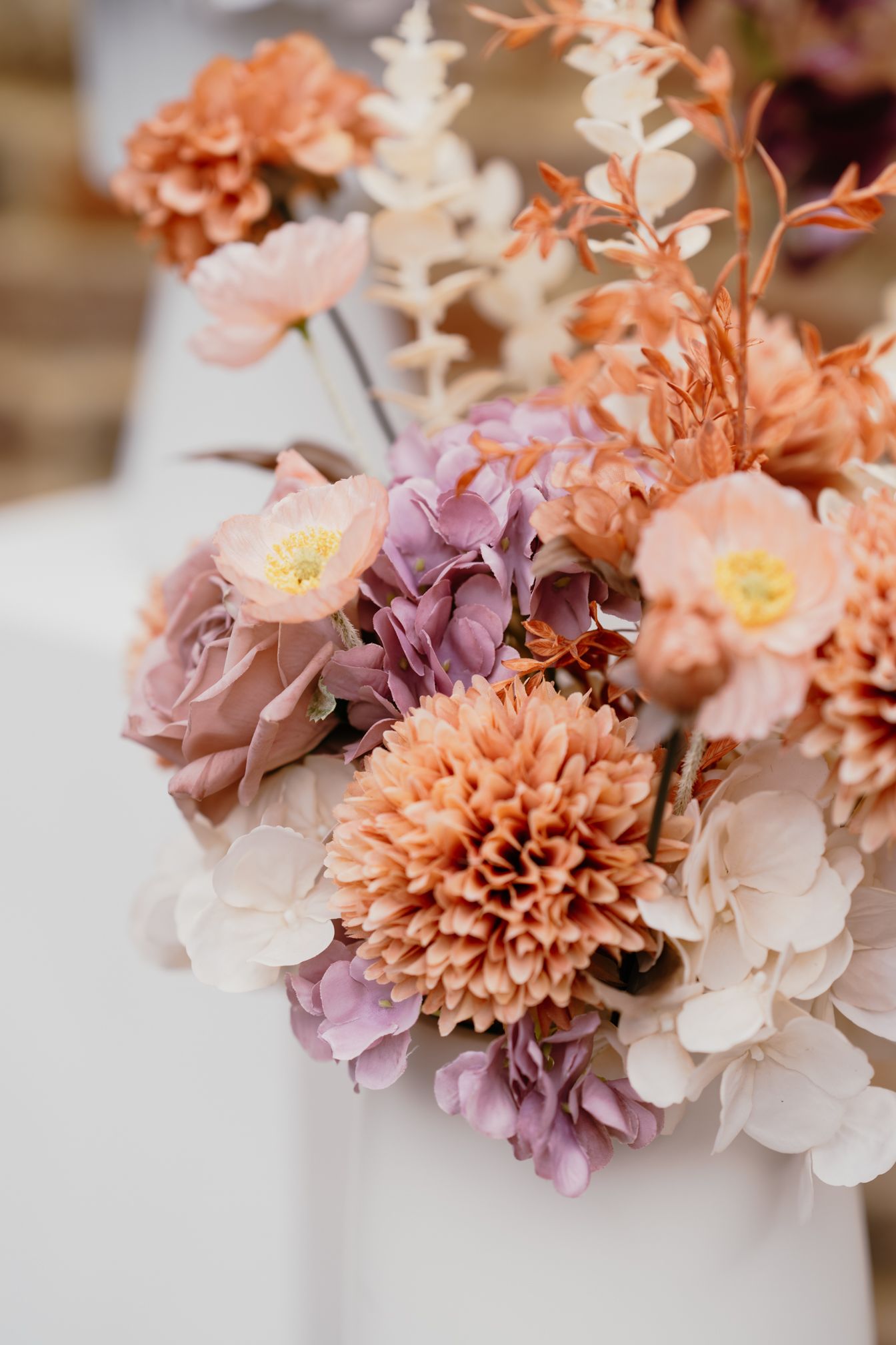 Delicate arrangement of peach and lavender flowers with soft petals against a light background.