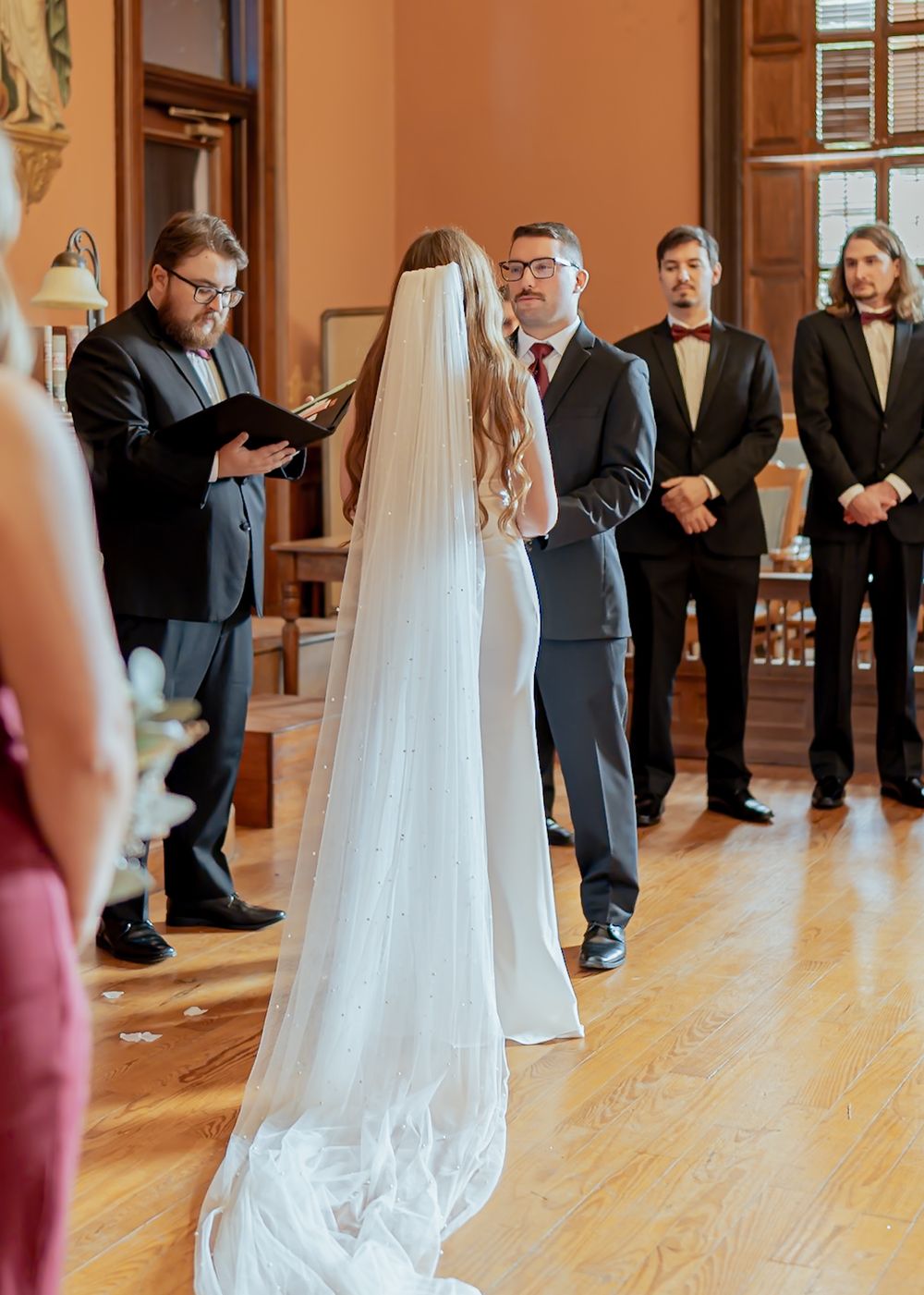 Wedding ceremony setup in an elegant room with hardwood floors and guests in formal attire.