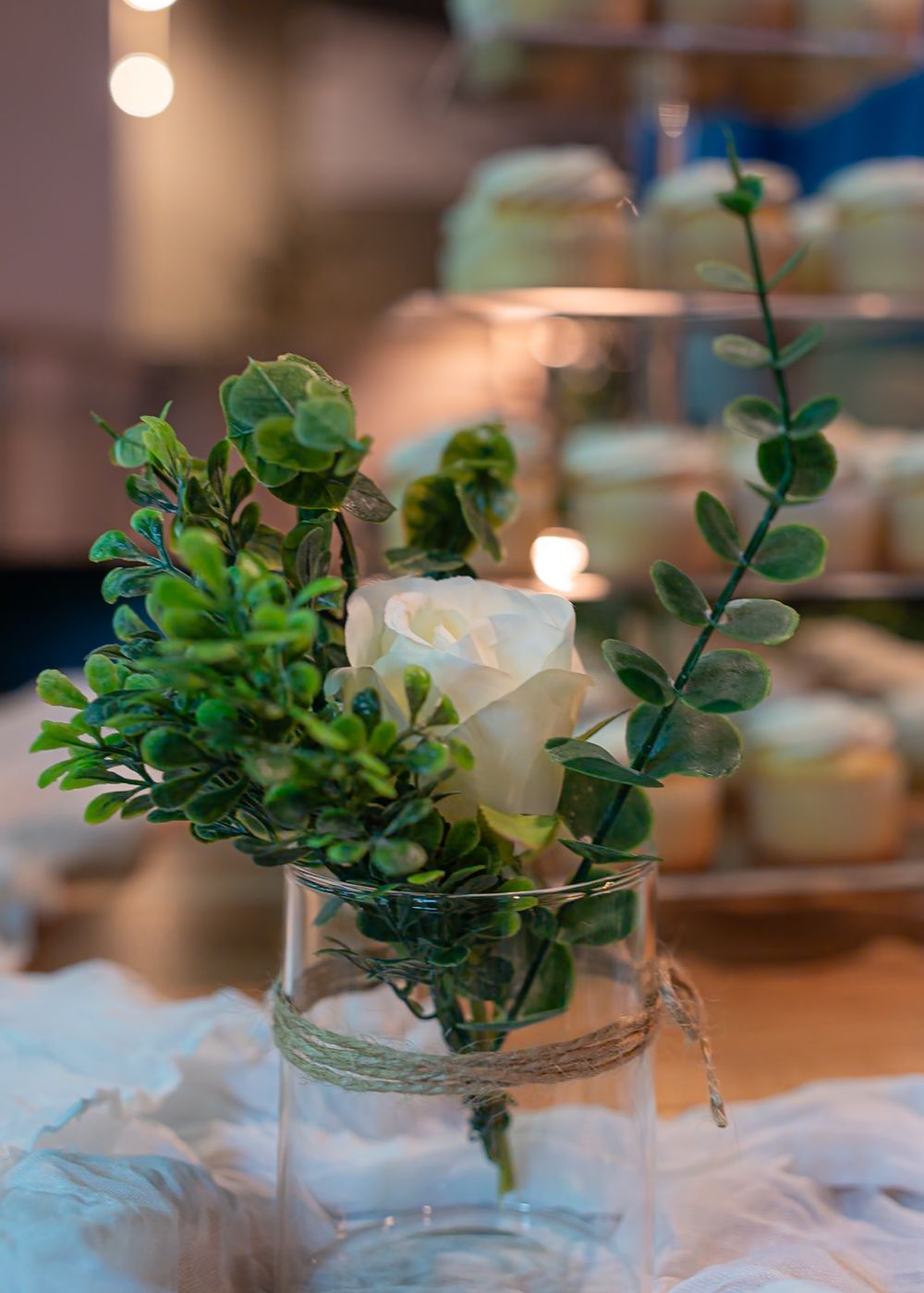 Simple centerpiece arrangements with greenery and white flowers in glass vases.
