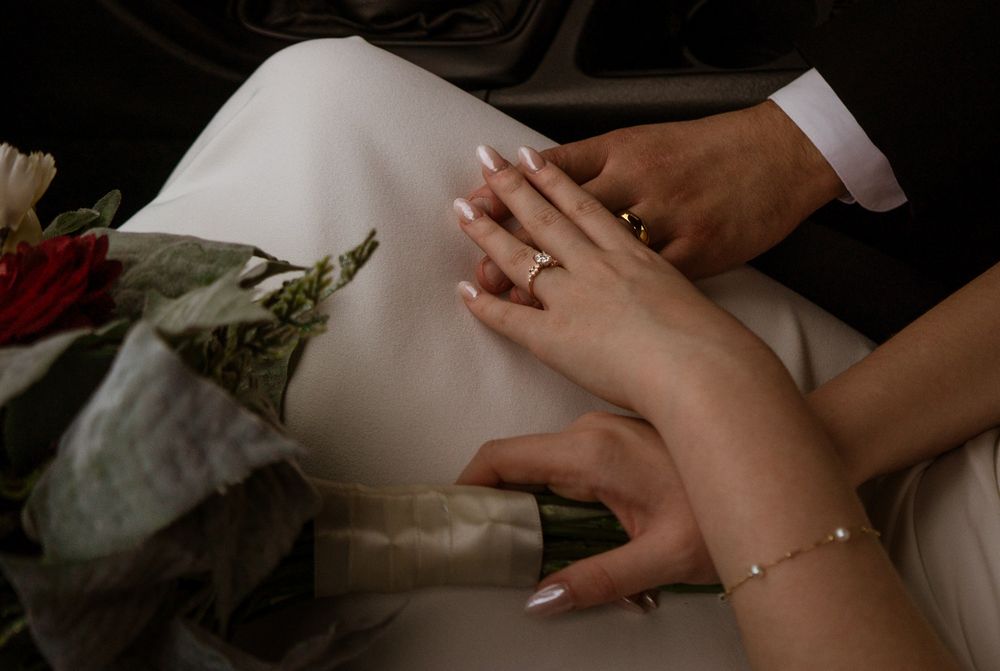 Close-up of hands with wedding rings and delicate jewelry against a white dress.
