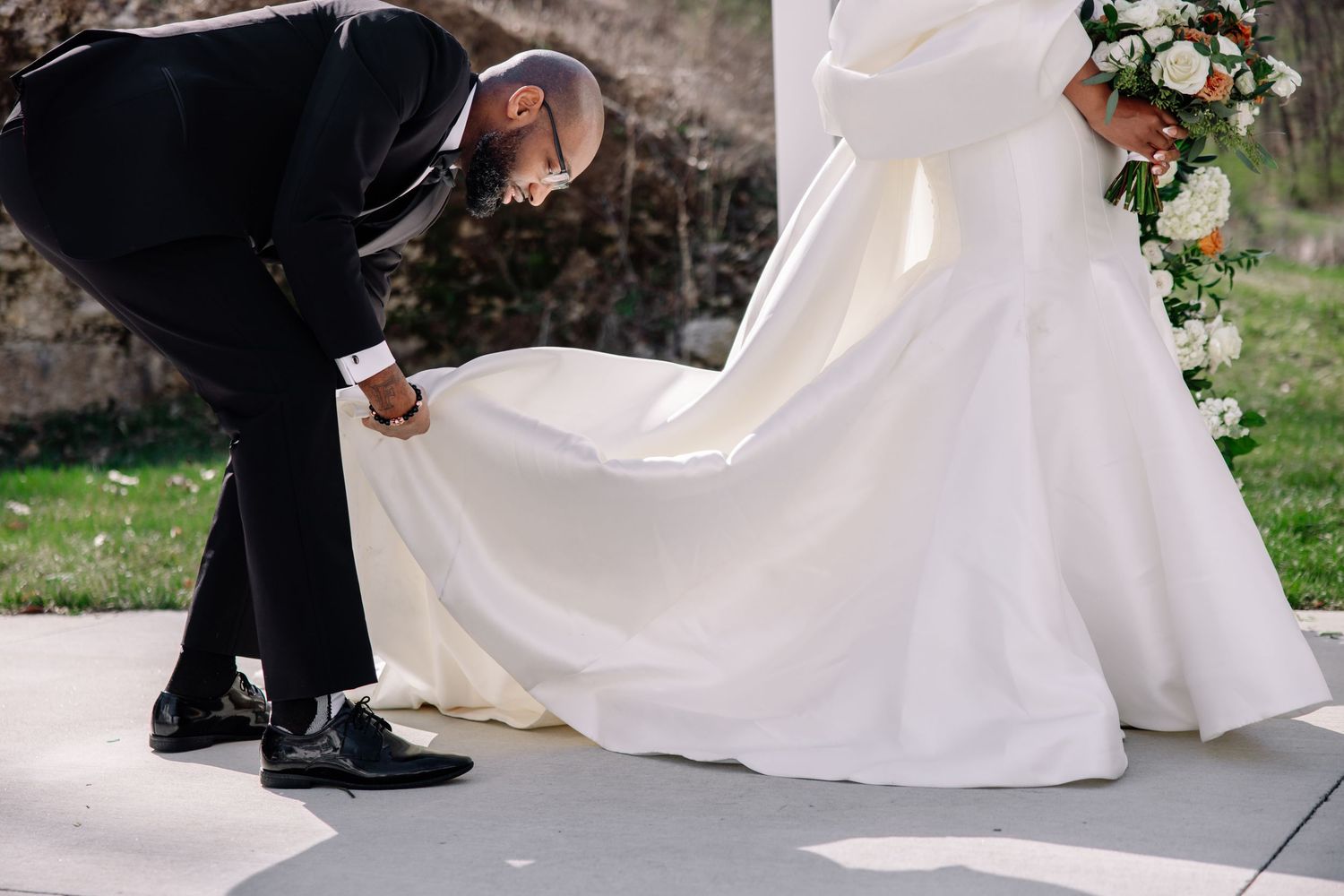 Wedding couple's feet visible beneath flowing white dress and black formal shoes.