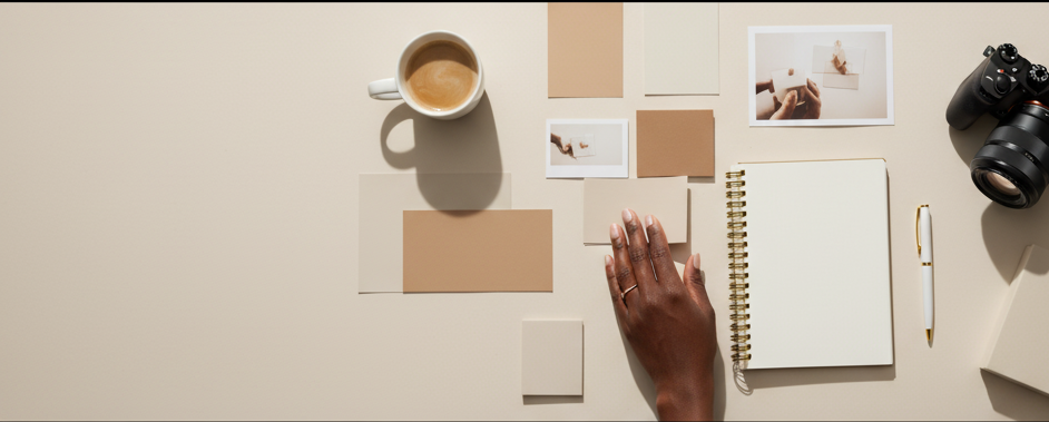 Vue de dessus d’un espace de travail avec une tasse de café, un carnet et des photos sur une surface blanche.