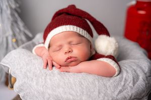 Sleeping newborn baby wearing red and white striped holiday hat rests on soft white blanket.