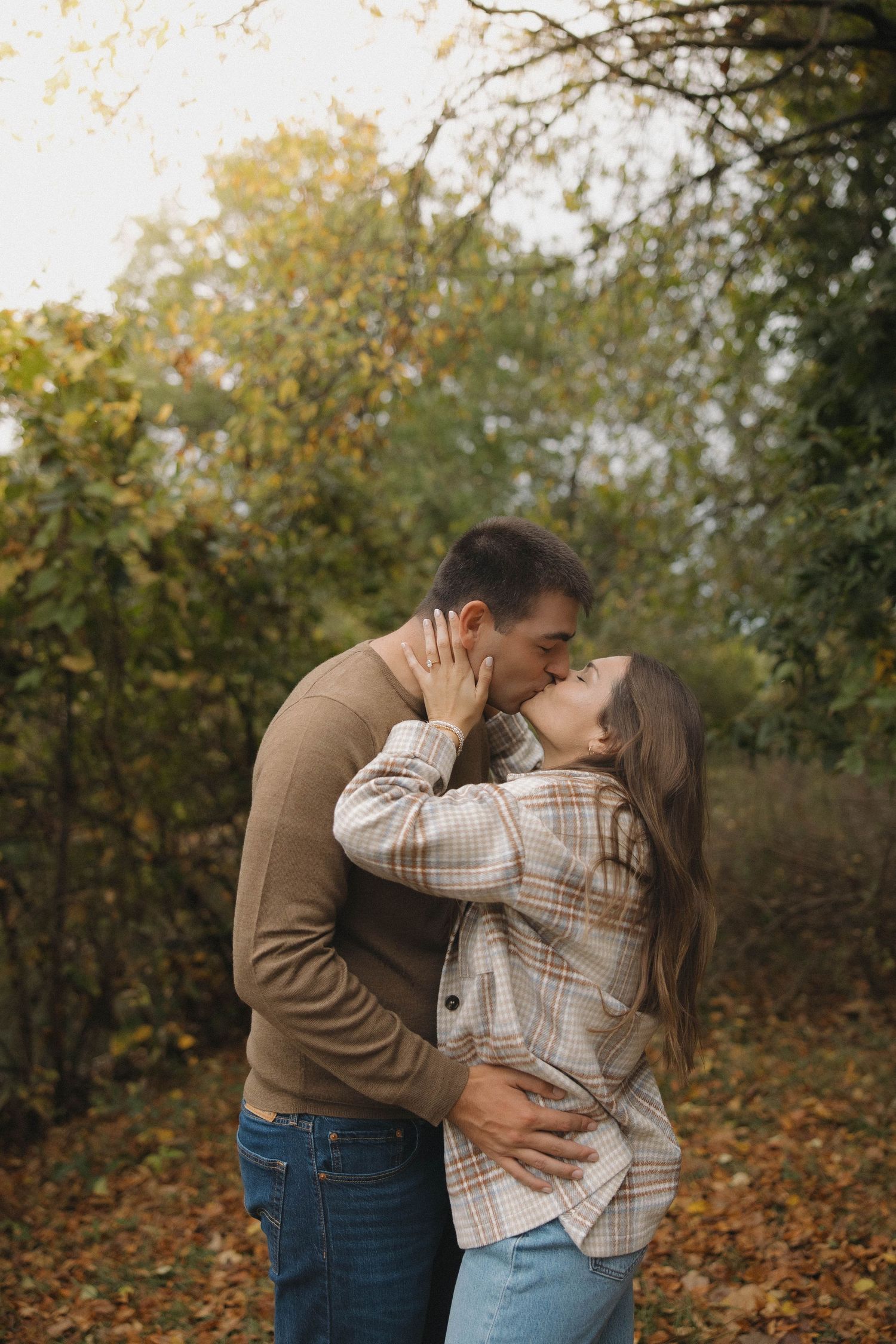 A couple embraces romantically among fall foliage and trees during an autumn photoshoot.