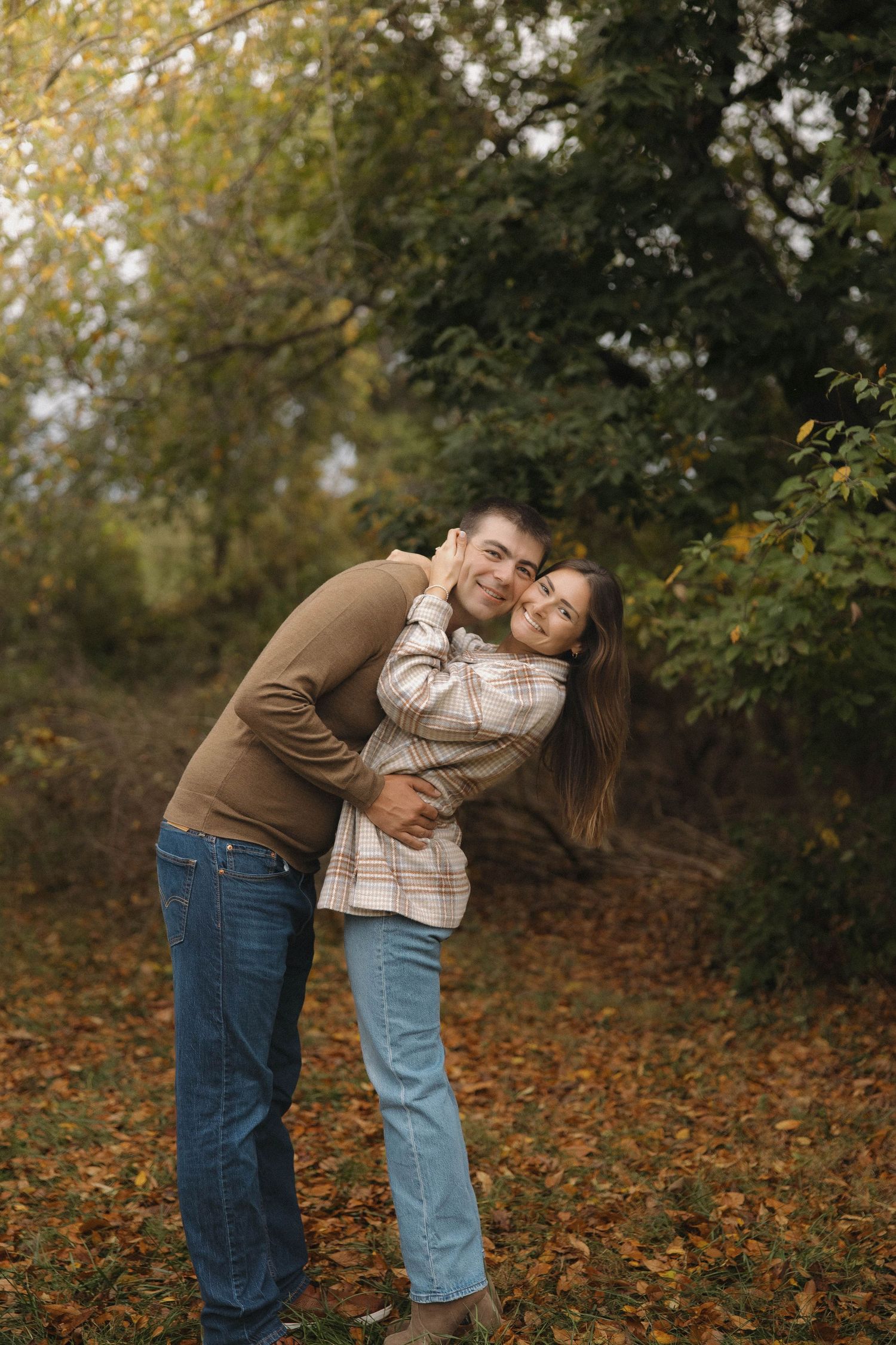 A couple shares tender moments among fallen autumn leaves in a wooded setting.