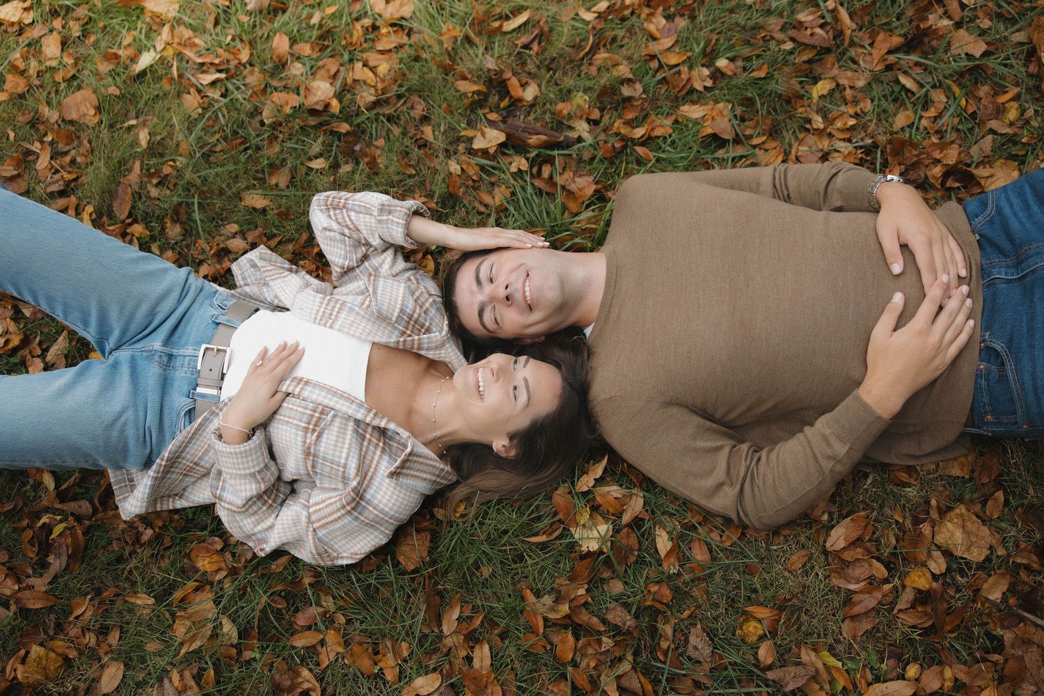 A couple lies together on autumn leaves during an intimate outdoor photo session.