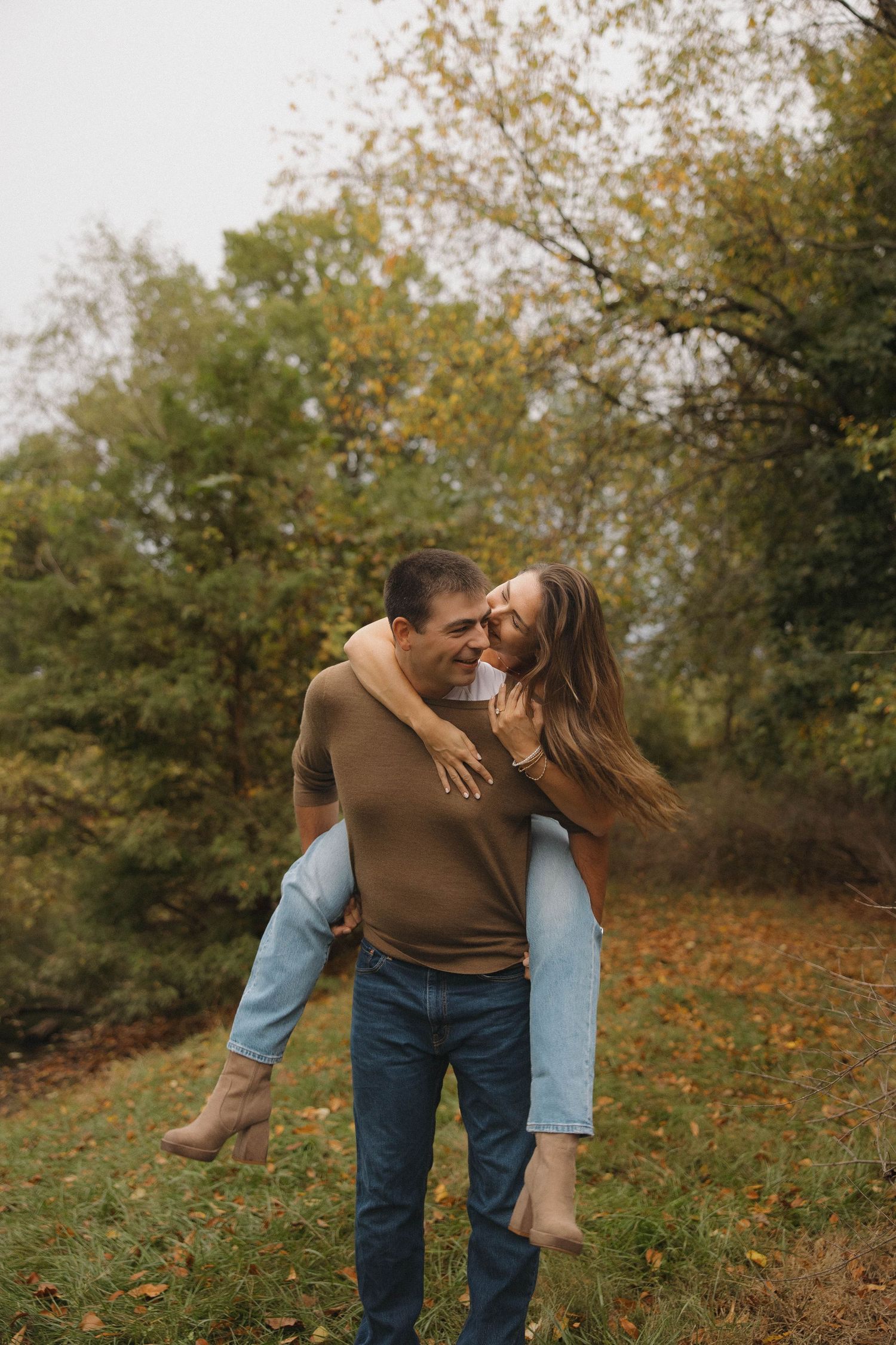 Playful autumn scene with couple embracing among fallen leaves and trees in warm autumn light.