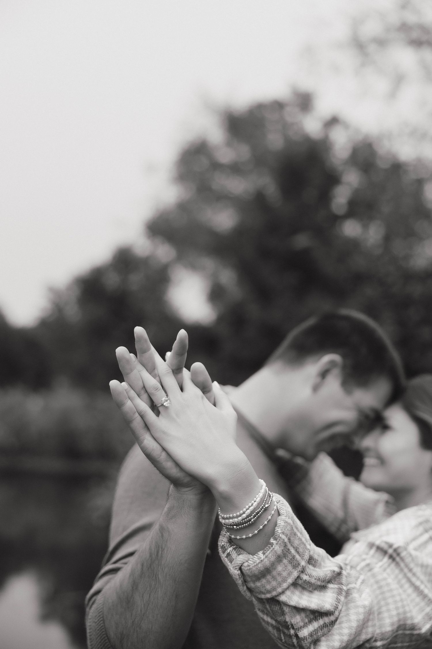 Black and white close-up of intertwined hands with an engagement ring, while a couple shares an intimate moment.