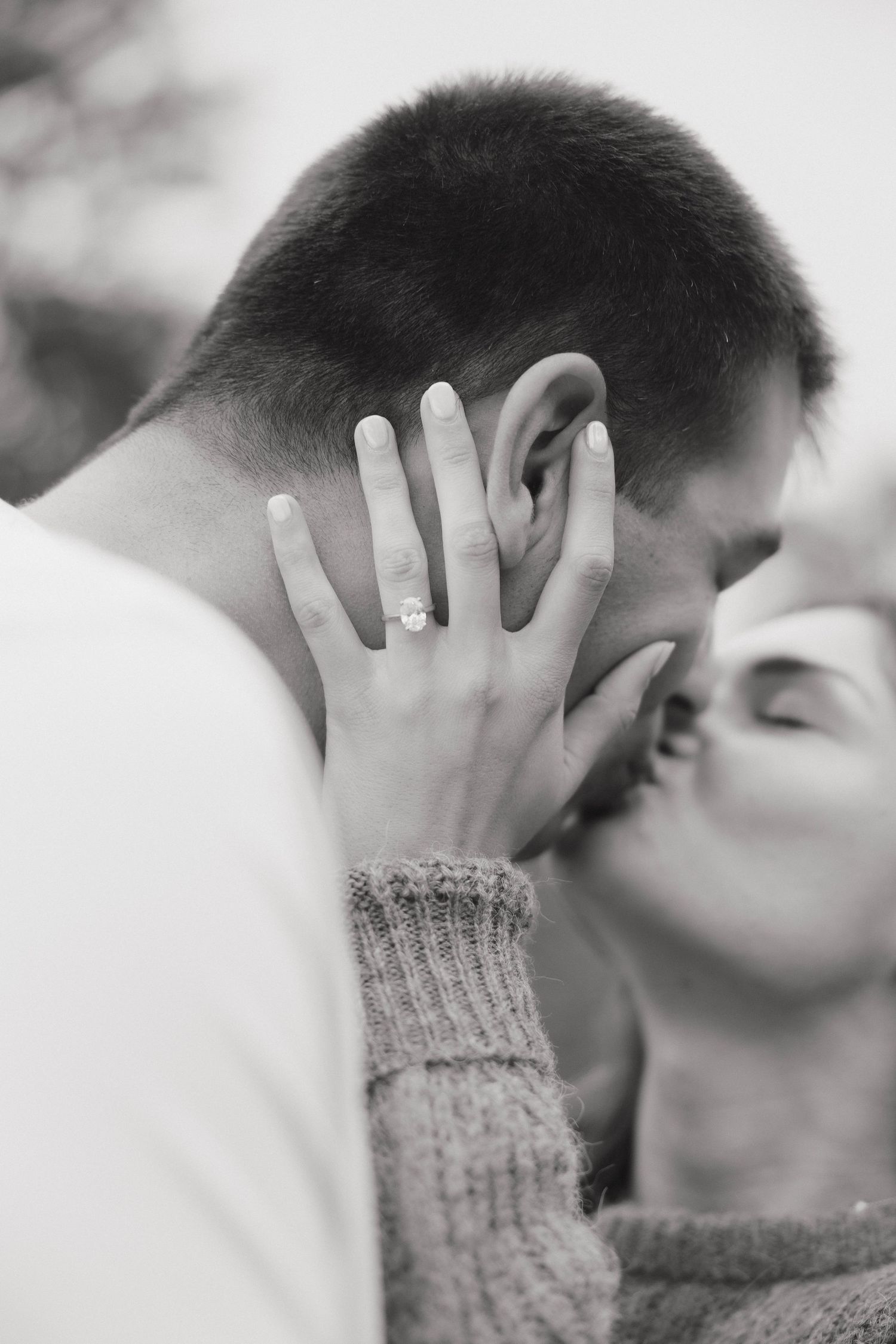 Black and white close-up of an intimate moment between a couple, with her hand showing an engagement ring.